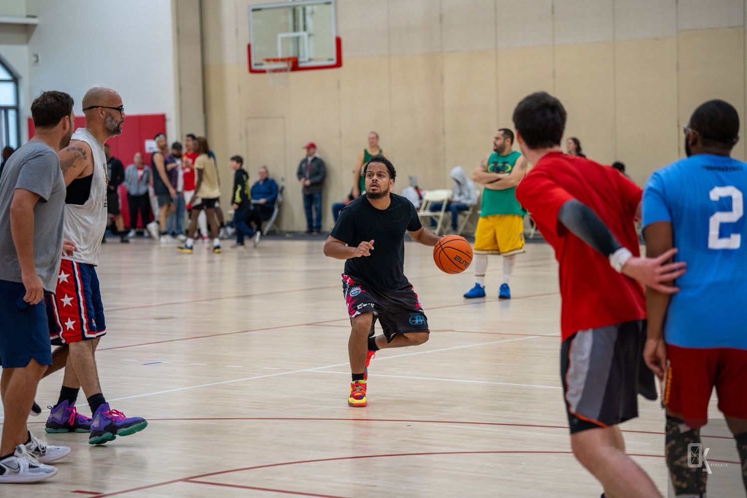 Basketball players compete during an indoor pickup game in a gymnasium with players wearing colorful jerseys.