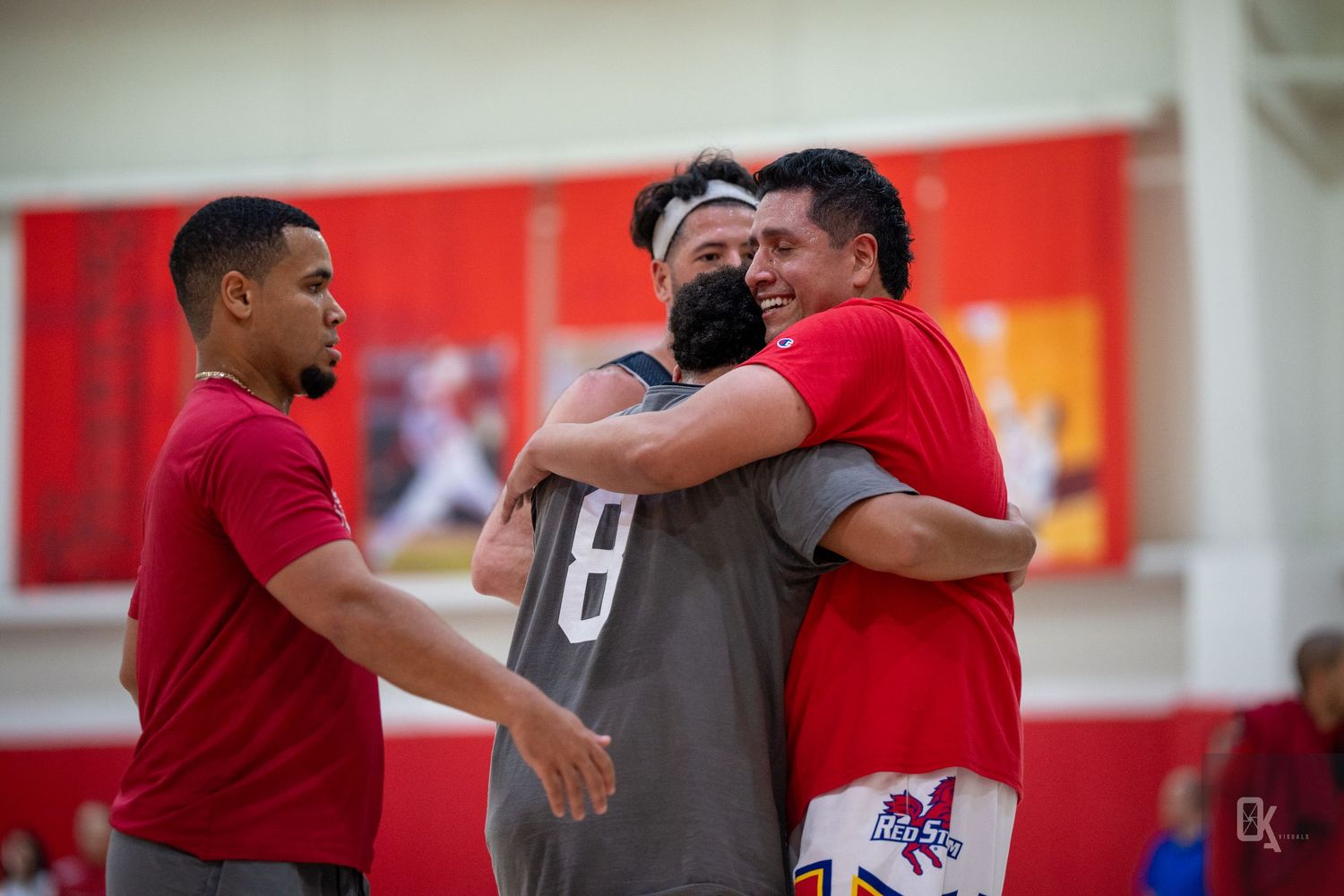 Basketball players in red jerseys celebrate with teammates and coaches after a game.