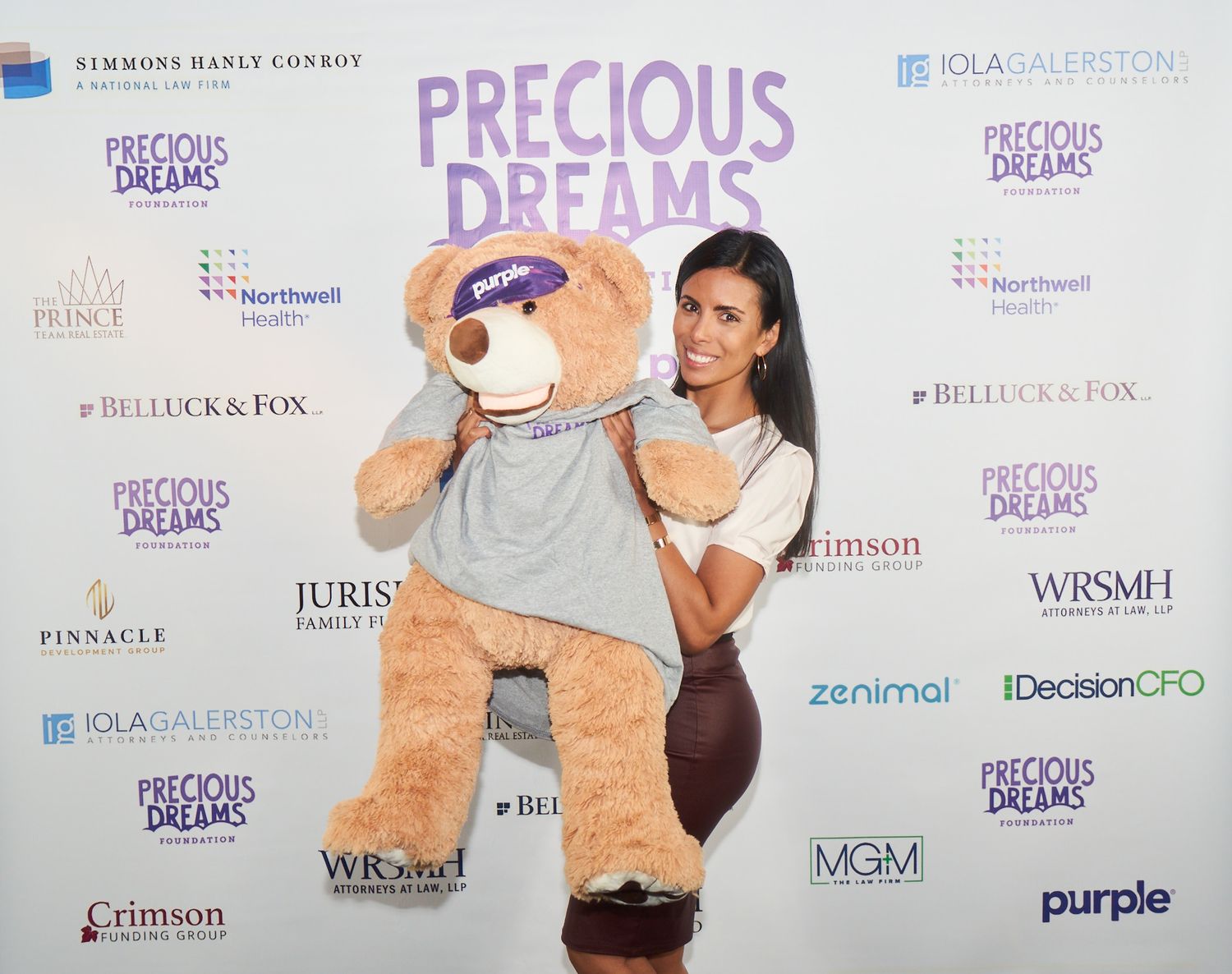 Step and repeat backdrop with sponsor logos at a Precious Dreams event displayed along a white wall.