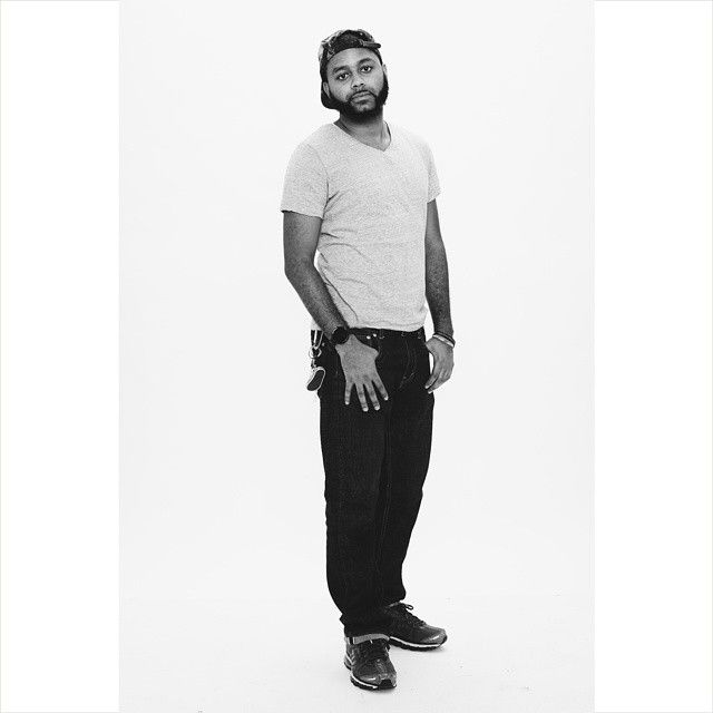 Black and white portrait of someone wearing a white t-shirt and dark pants posing against a plain background.