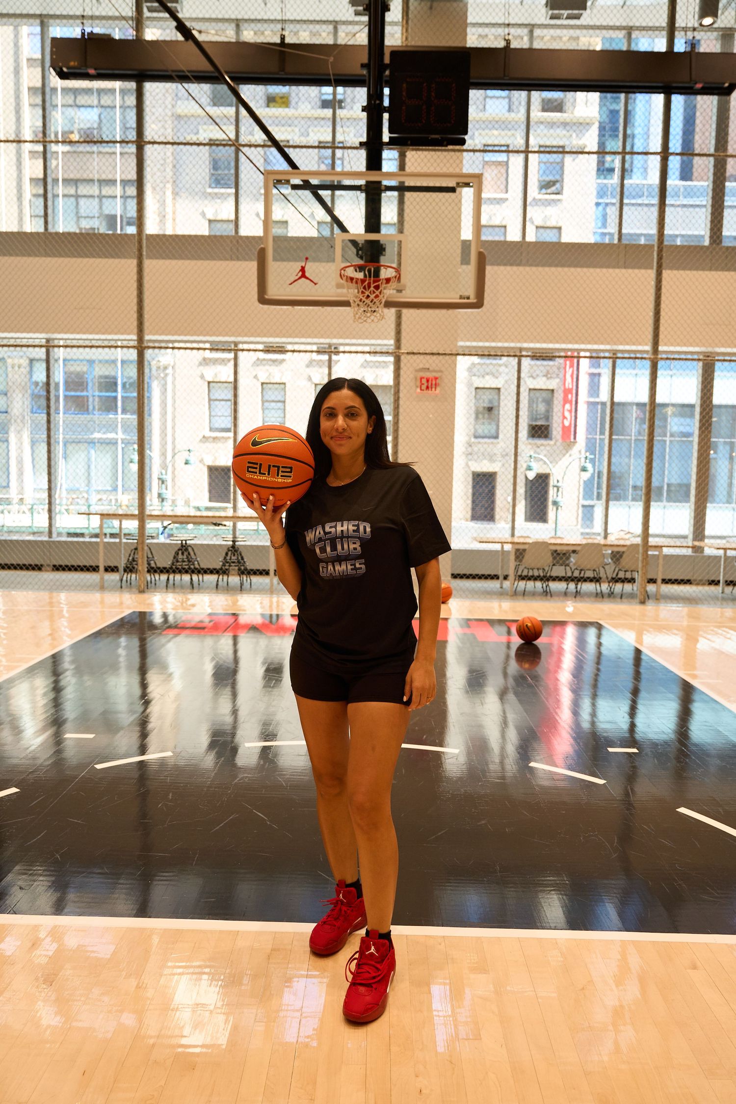 Athlete in a black t-shirt and red sneakers performing jump shots on a glossy indoor basketball court.
