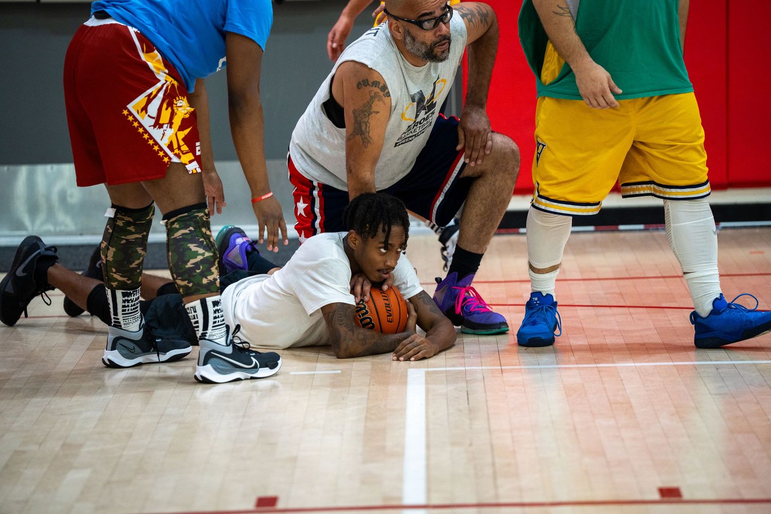 Basketball players wearing colorful shoes and uniforms practice dribbling drills on a gym court during training.