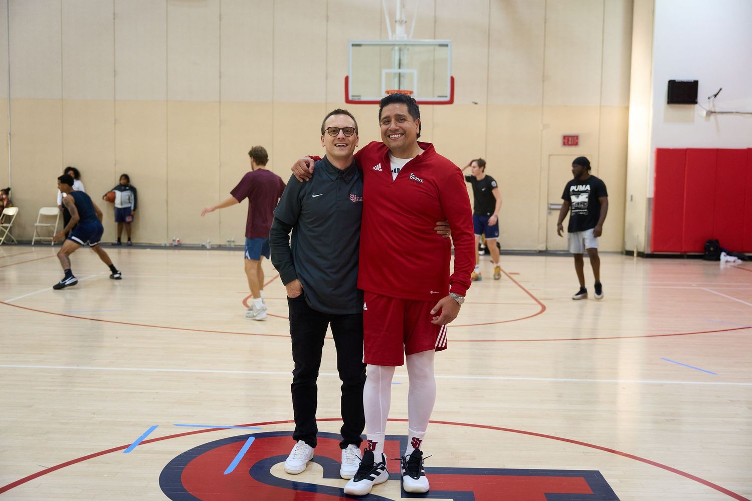 Two people posing together on a basketball court with red and white decorative elements.