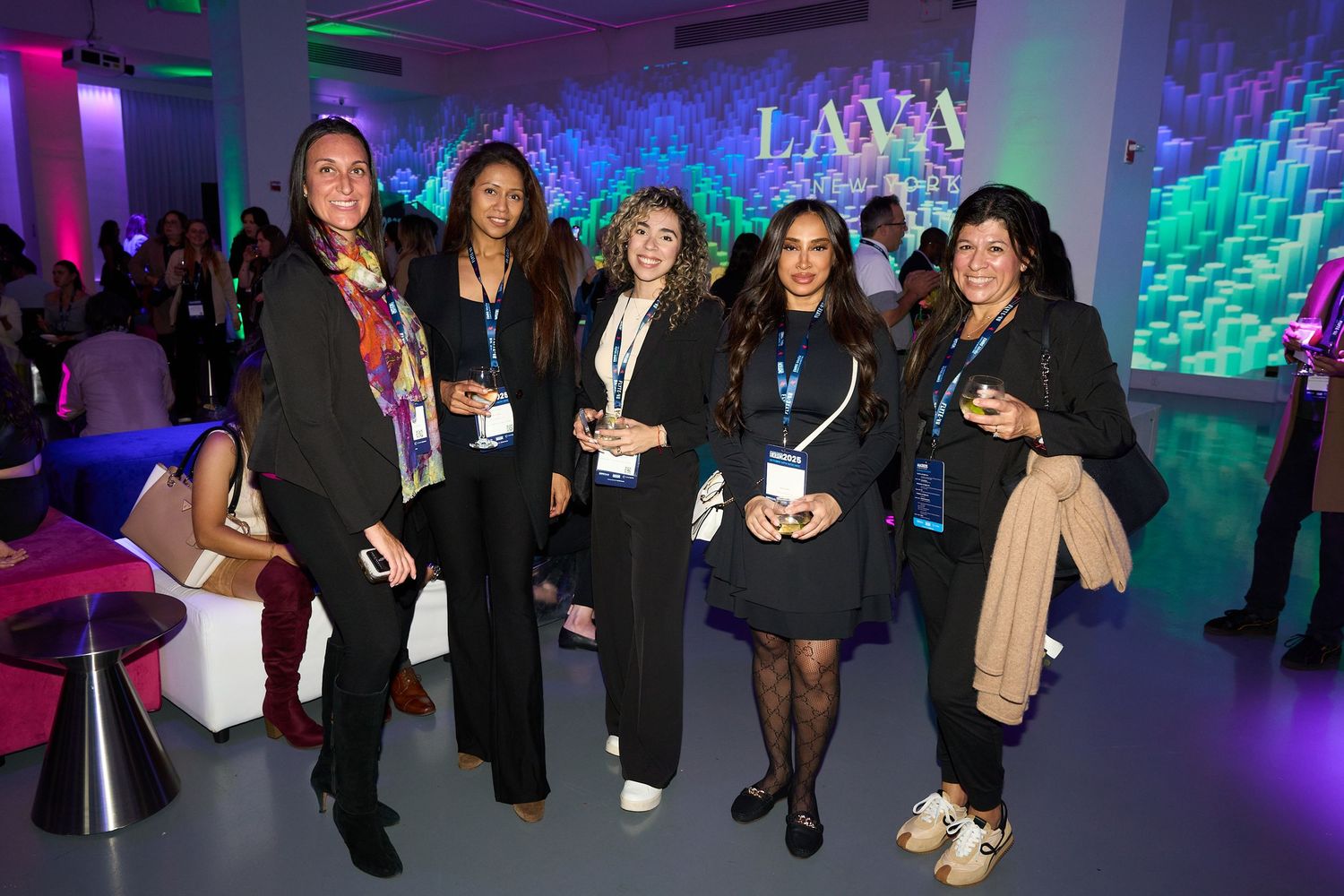 People networking and socializing at a business event with colorful blue and purple lighting in the background.