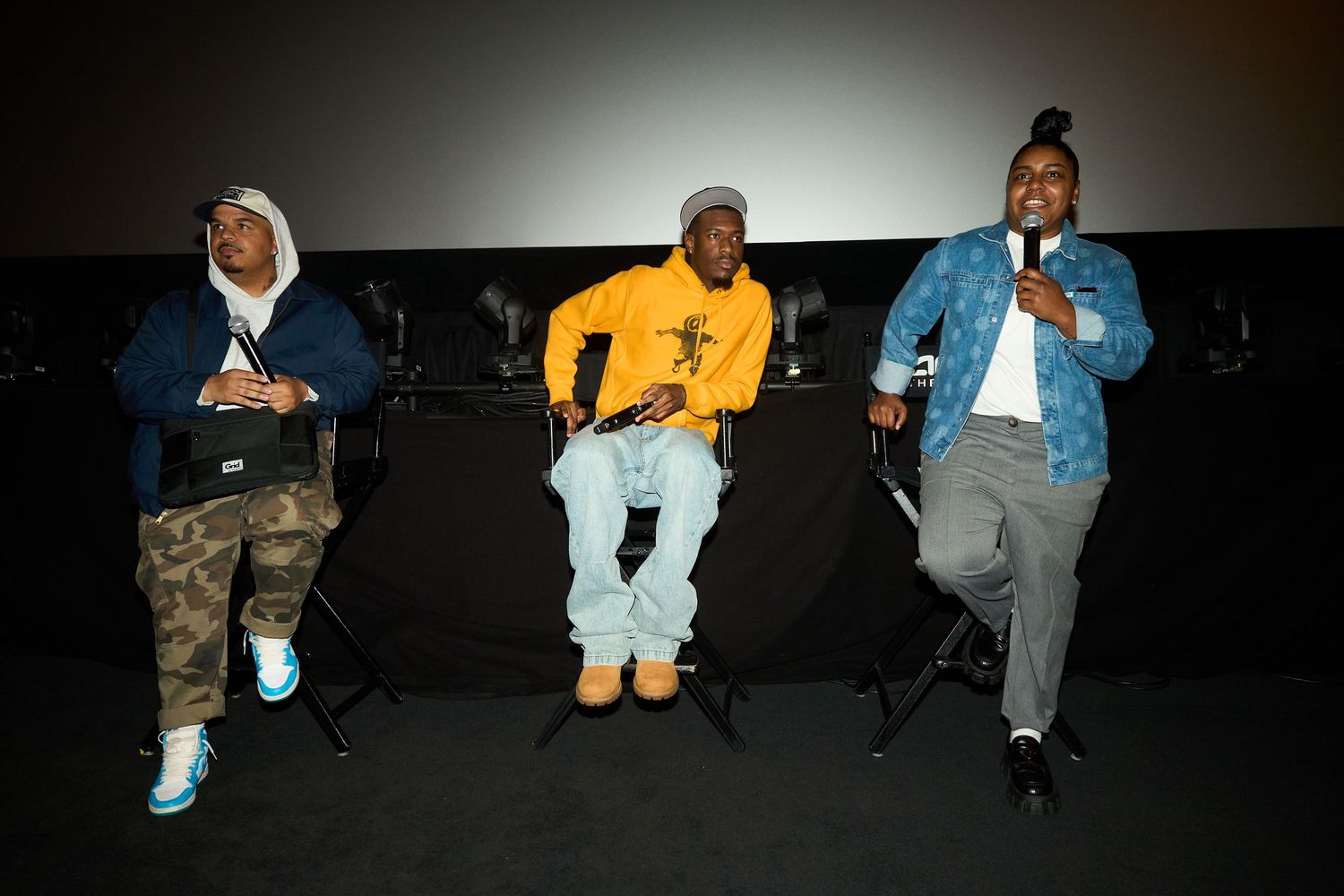 Three men seated on stage at a panel event, dressed in colorful streetwear, speaking into a microphone.