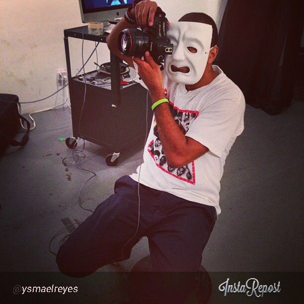 Photographer wearing a white mask holds camera equipment during a studio shoot.