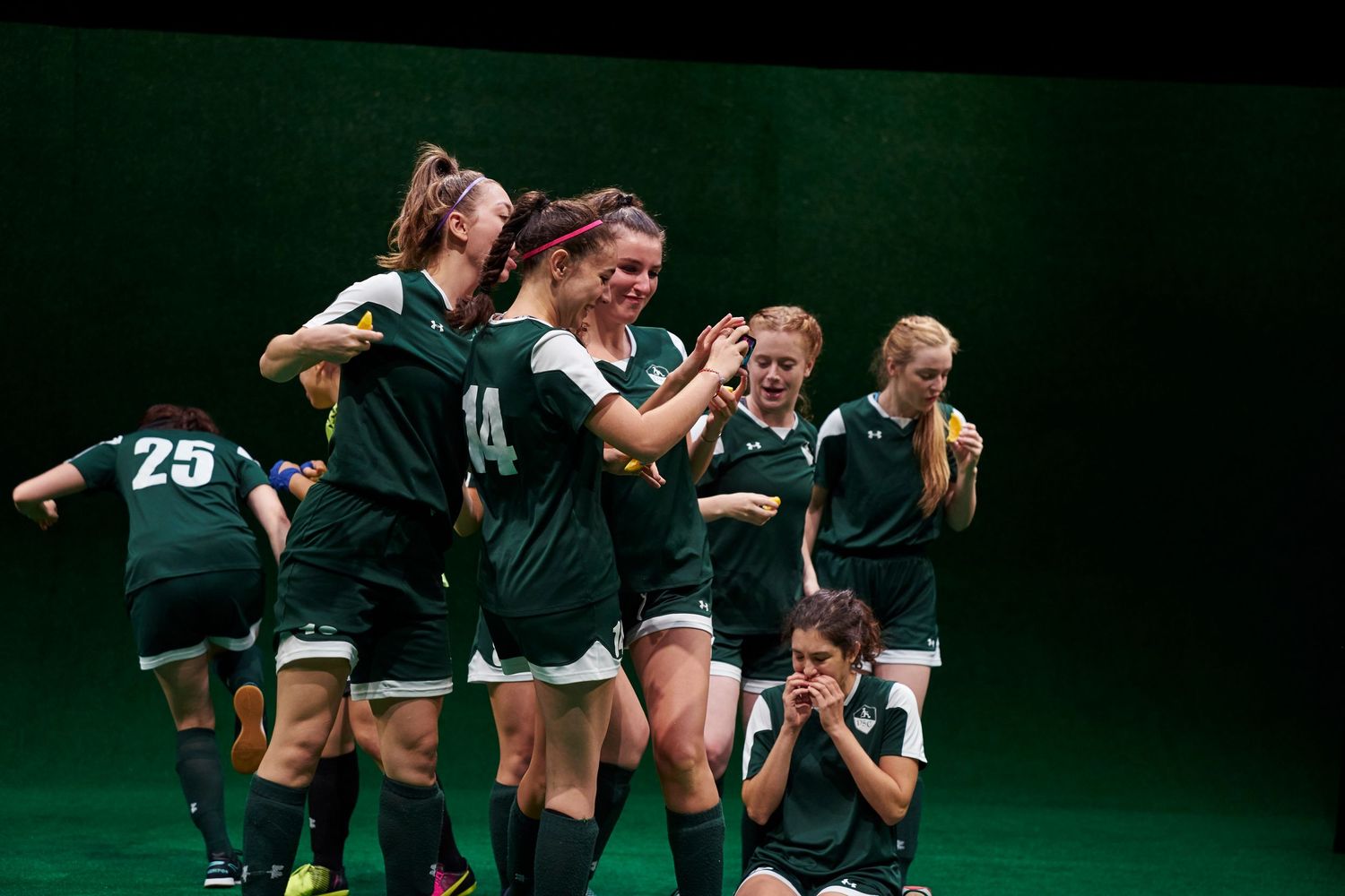 Athletes in green jerseys celebrate together on a dark stage with dramatic lighting during a team performance.