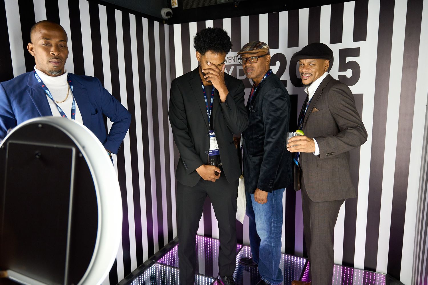 People in formal attire stand in front of a black and white striped backdrop at an event.