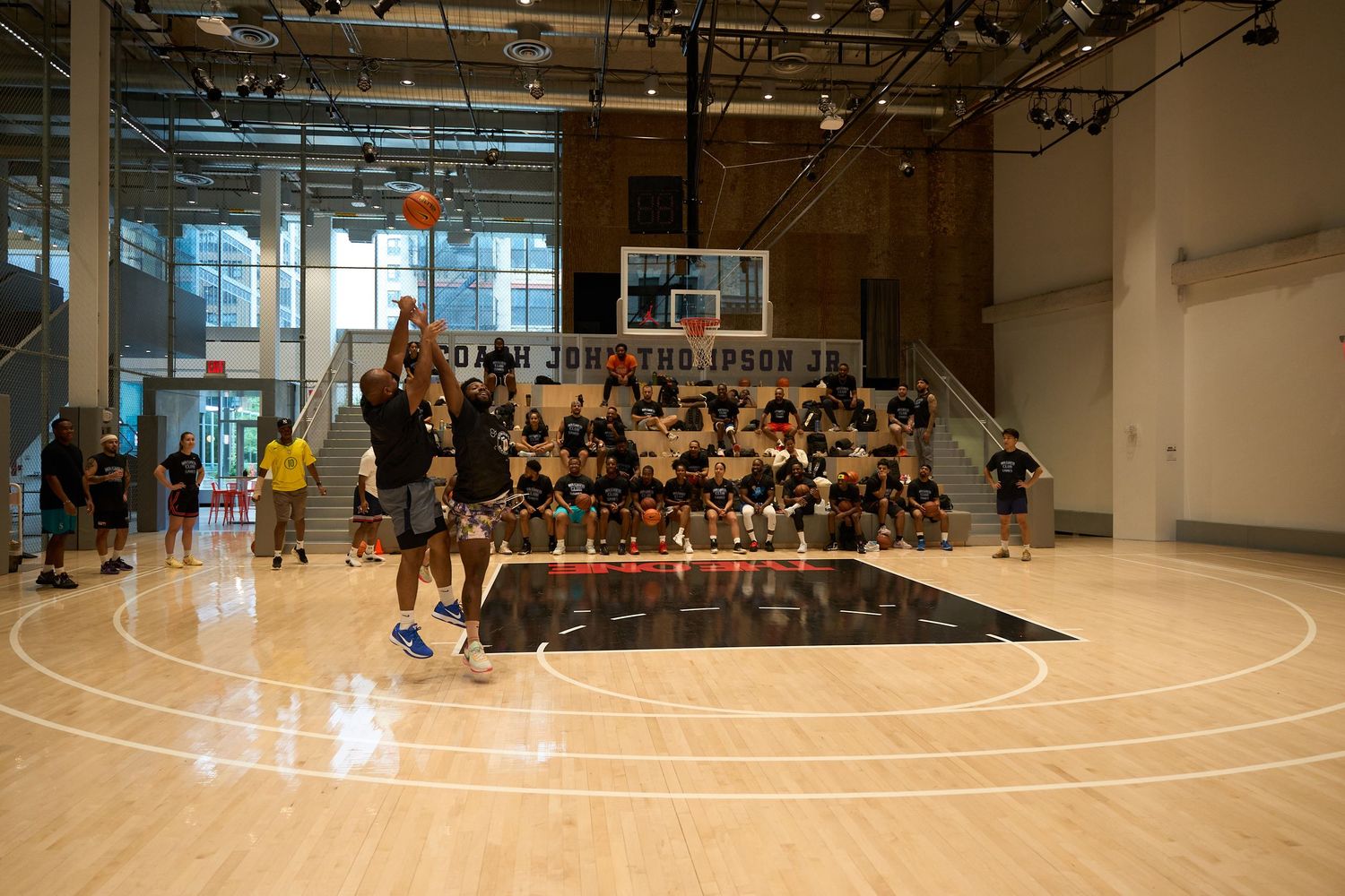 Wide angle view of a basketball court with spectators seated along the sidelines during practice session.