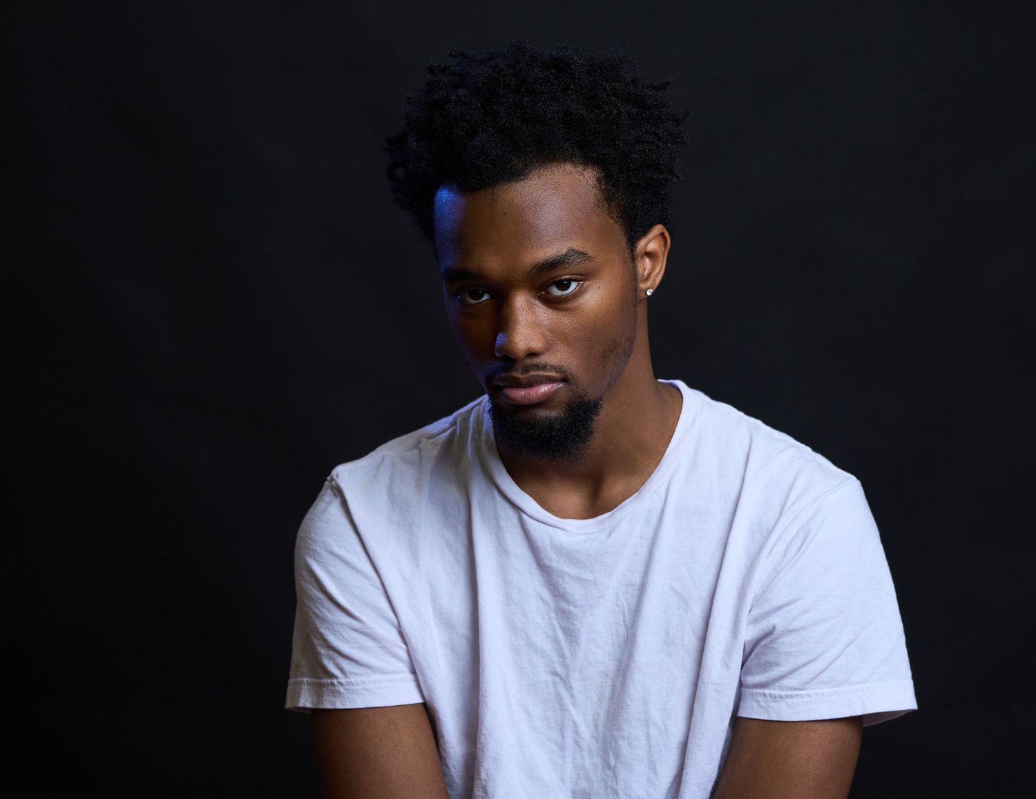 Portrait of person wearing white t-shirt against dark background with dramatic studio lighting.