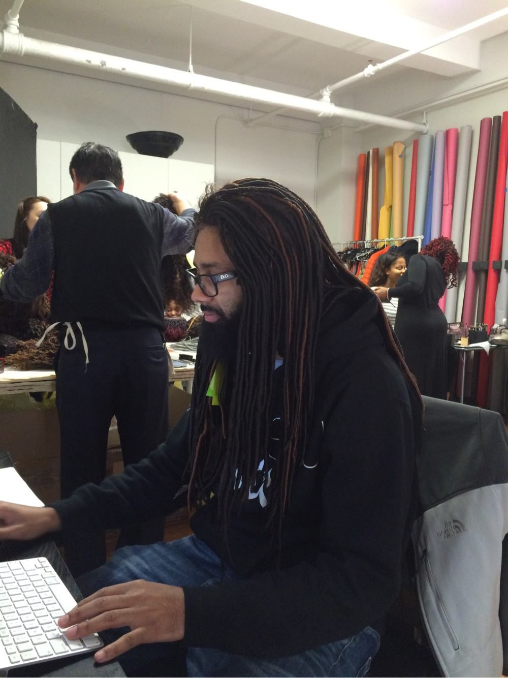 Student works on laptop in classroom with colorful striped wall decor visible in background.