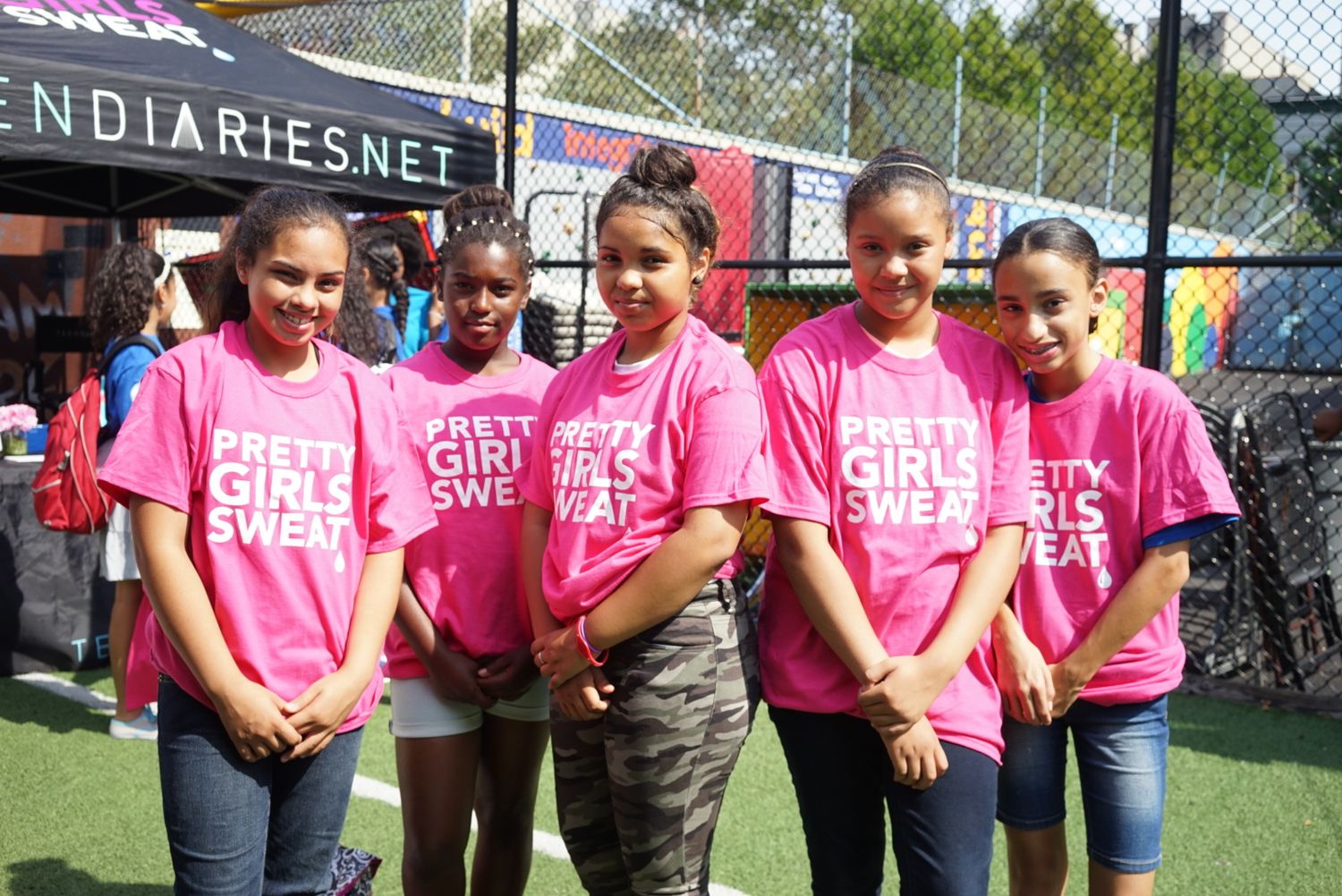 Group wearing matching pink t-shirts poses together at outdoor sports facility.