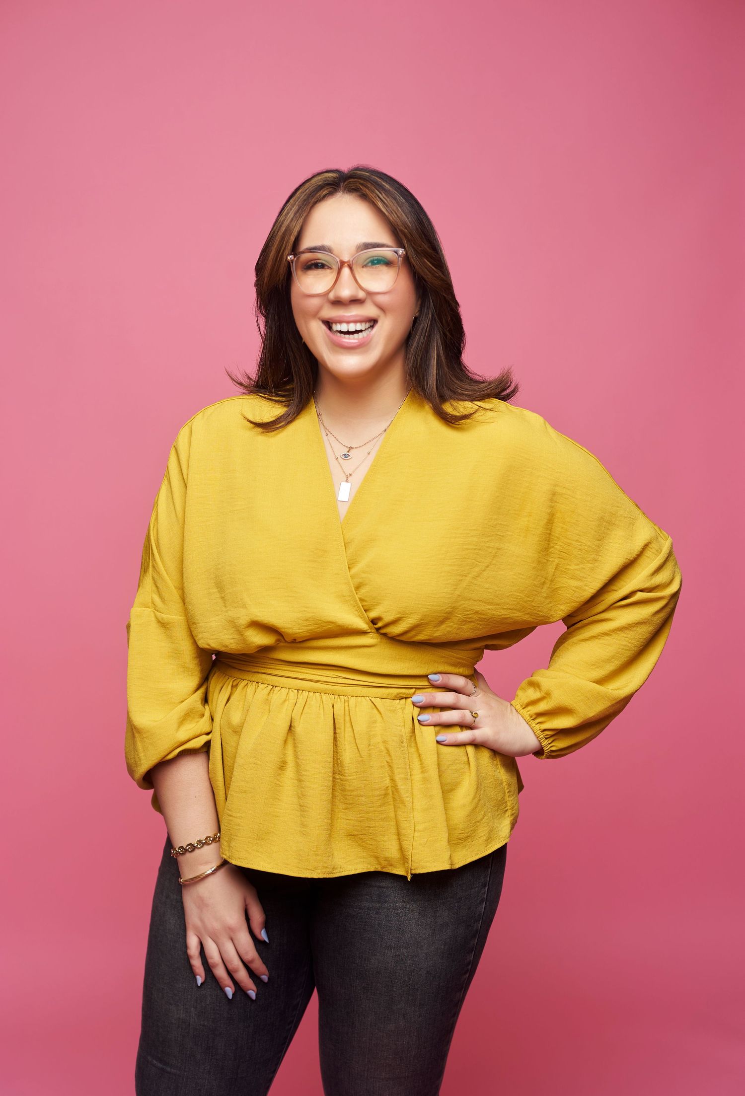 Model in mustard yellow wrap top and dark denim jeans poses against pink backdrop in four fashion portraits.
