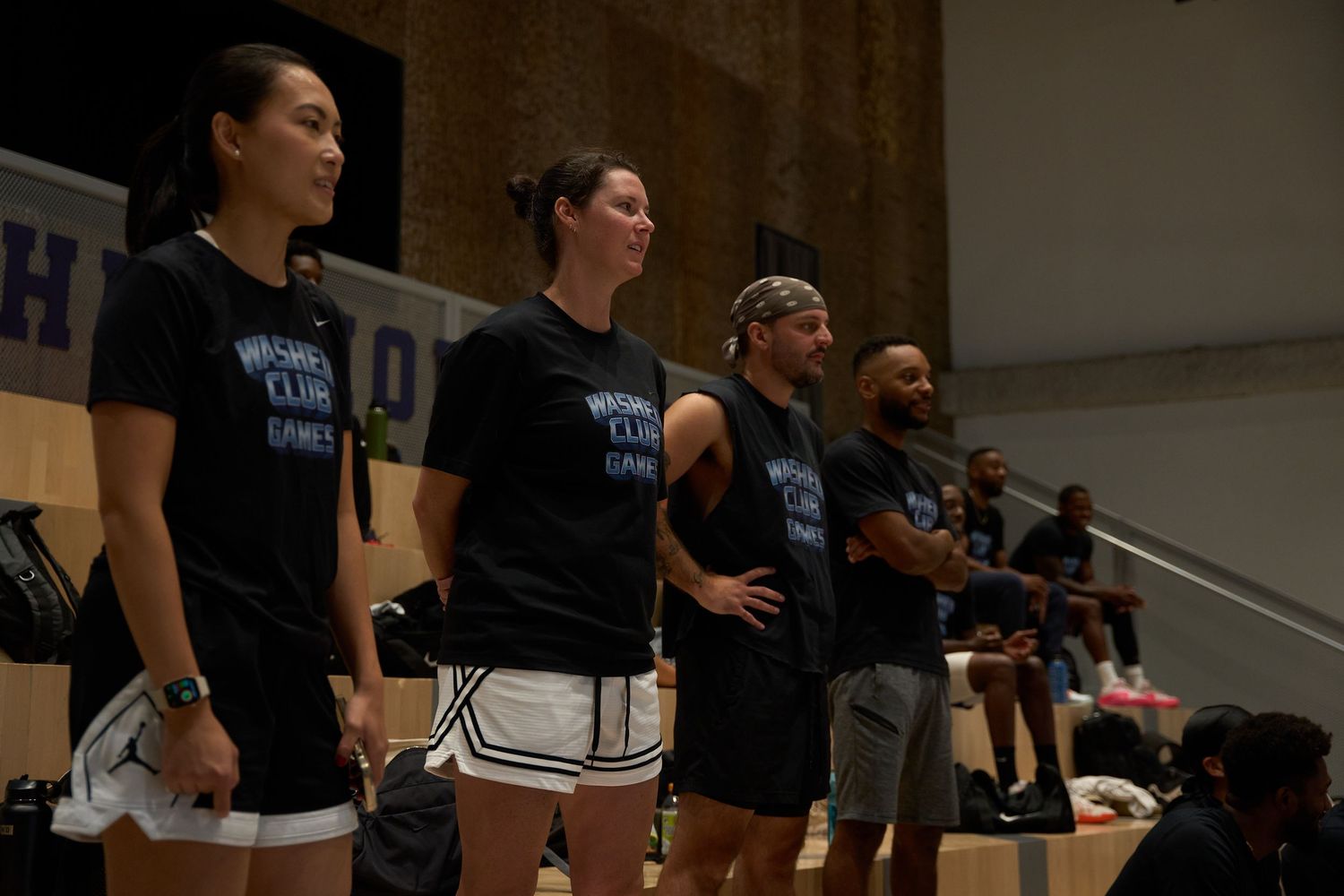 Basketball players in black jerseys gather on the court during an indoor game.