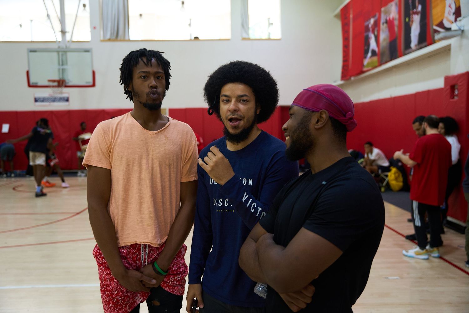 Three friends chatting together in a basketball gymnasium with red walls.