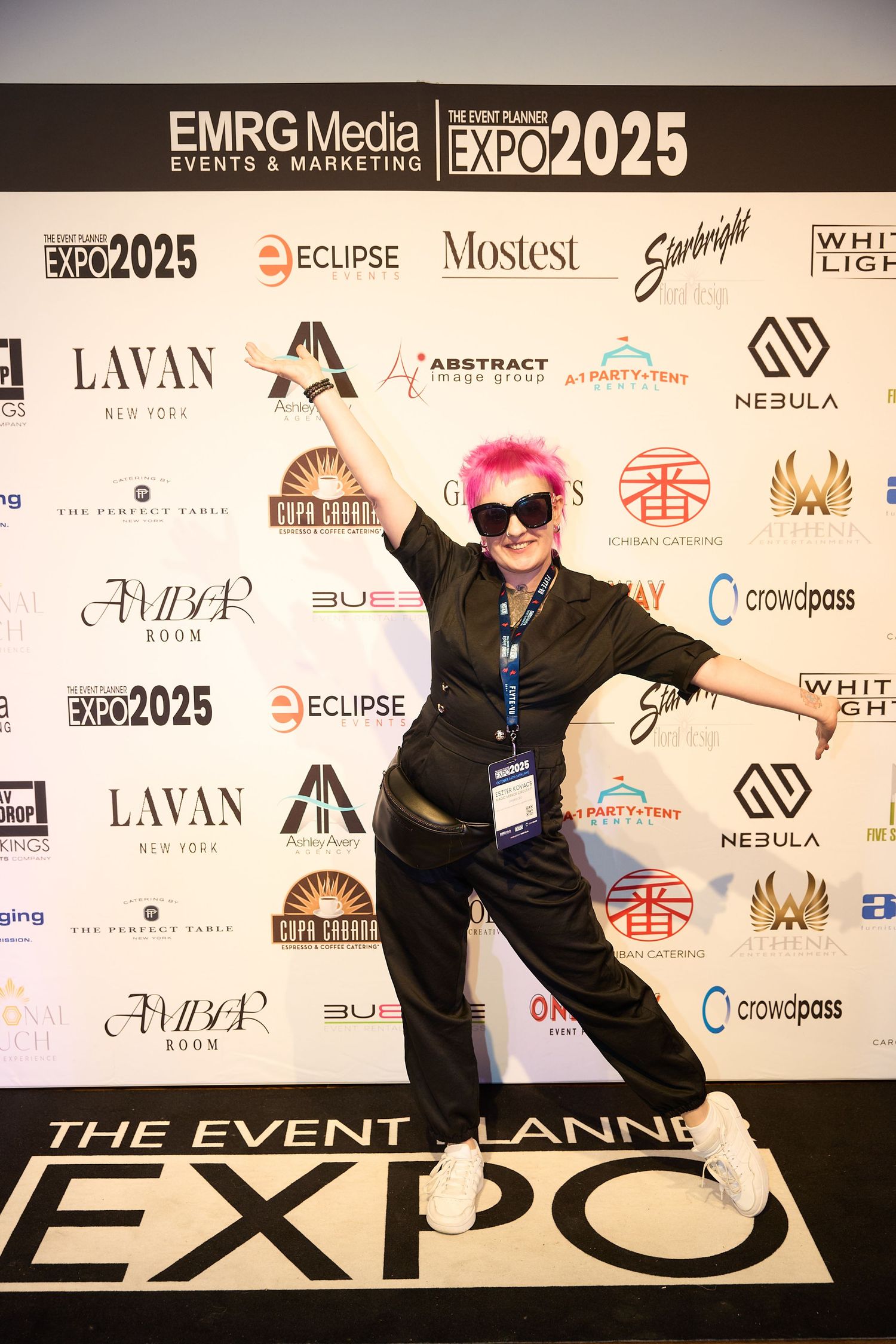 Person in black outfit poses energetically against event backdrop with multiple sponsor logos at The Event Planner Expo 2025.