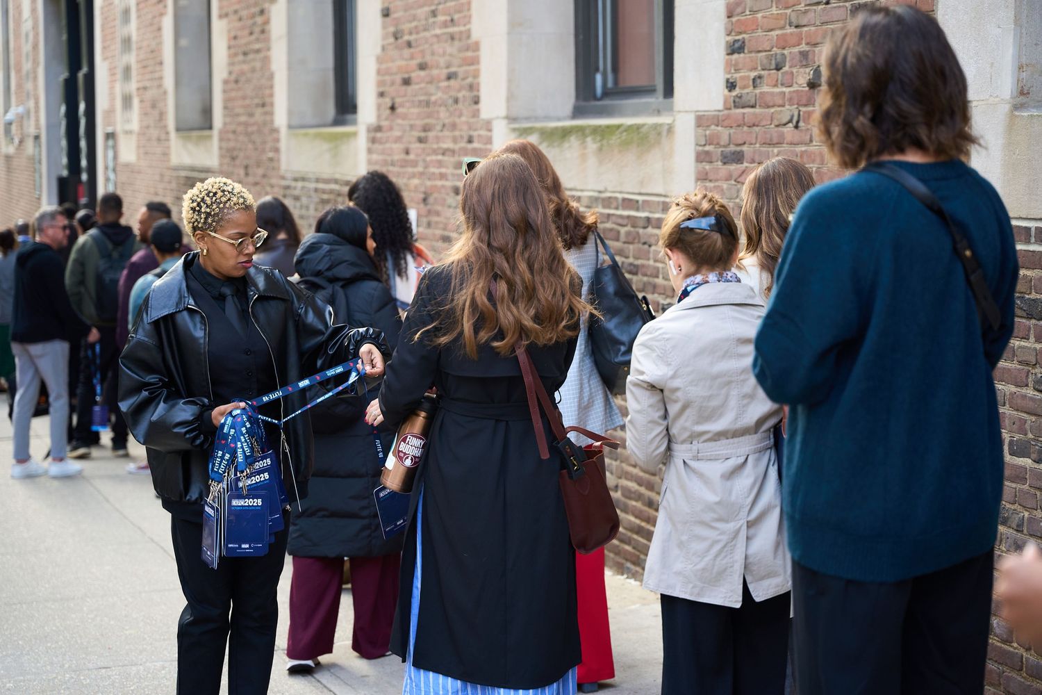 A line of people wait outside a brick building entrance during a daytime event.