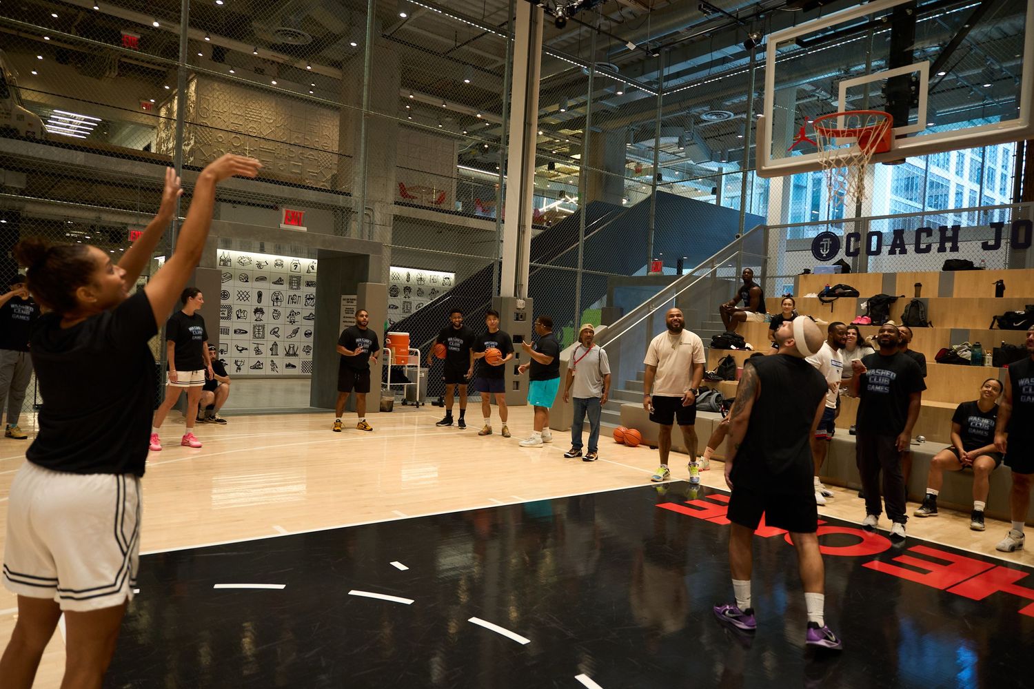 Basketball players practicing drills on an indoor court during a training session with multiple hoops visible.