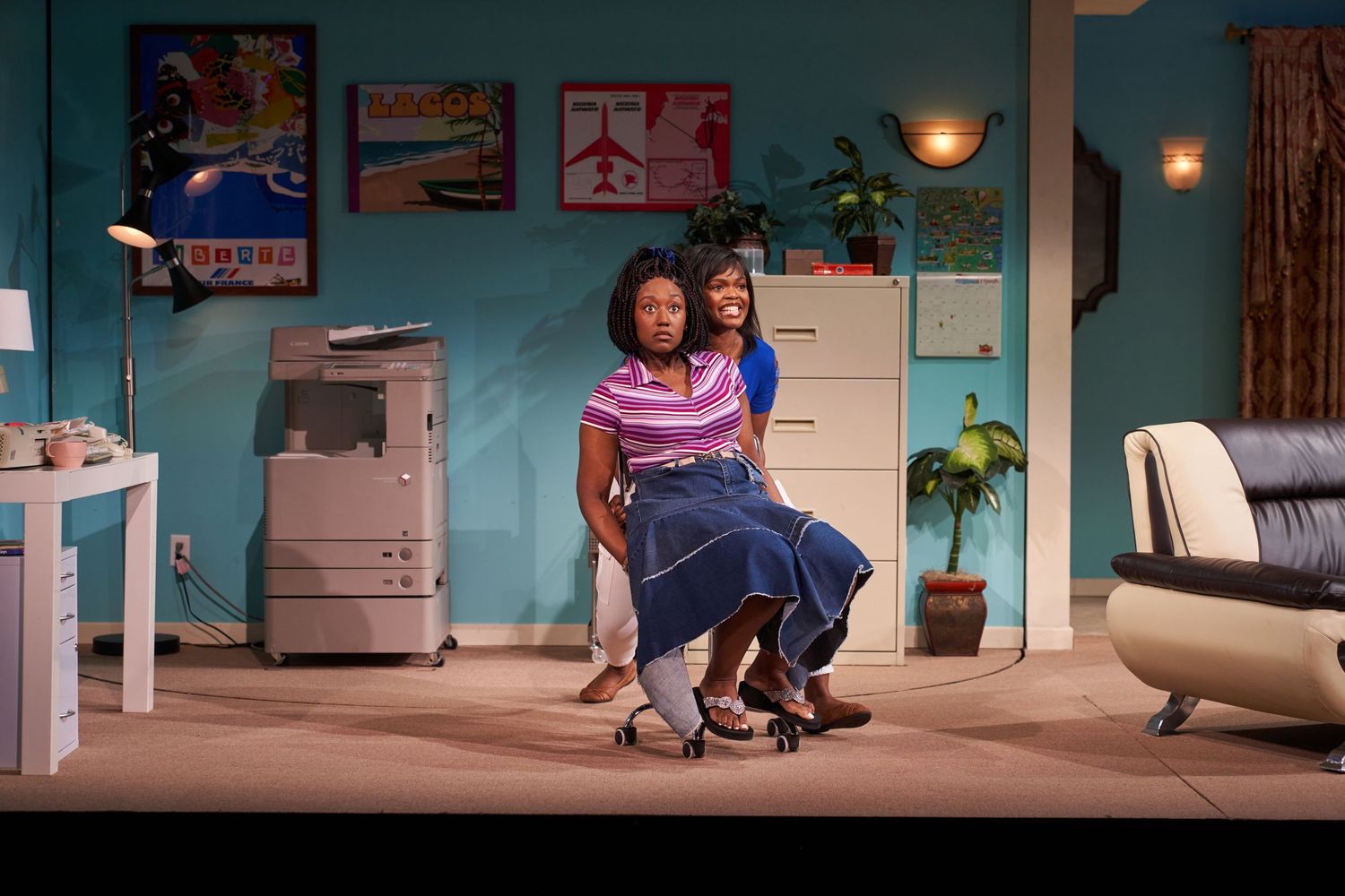 Two individuals share a moment together on stage in a home office setting with turquoise walls and office furniture.