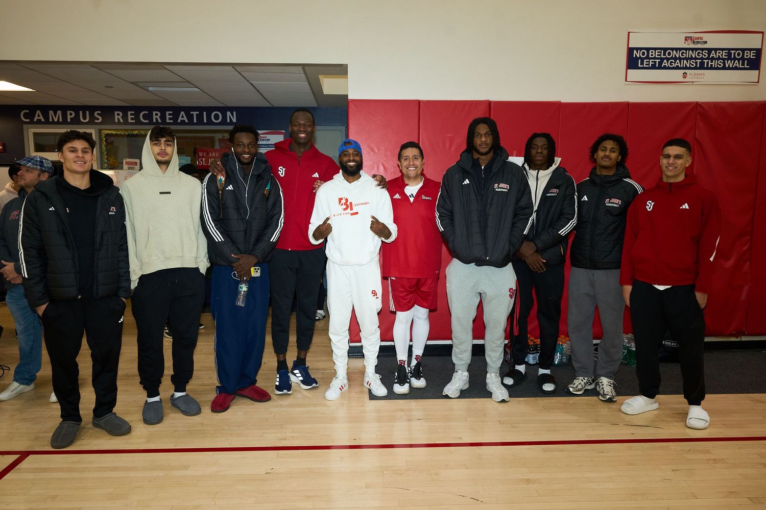 Group of athletes lined up against a red wall in a gymnasium during a basketball event.
