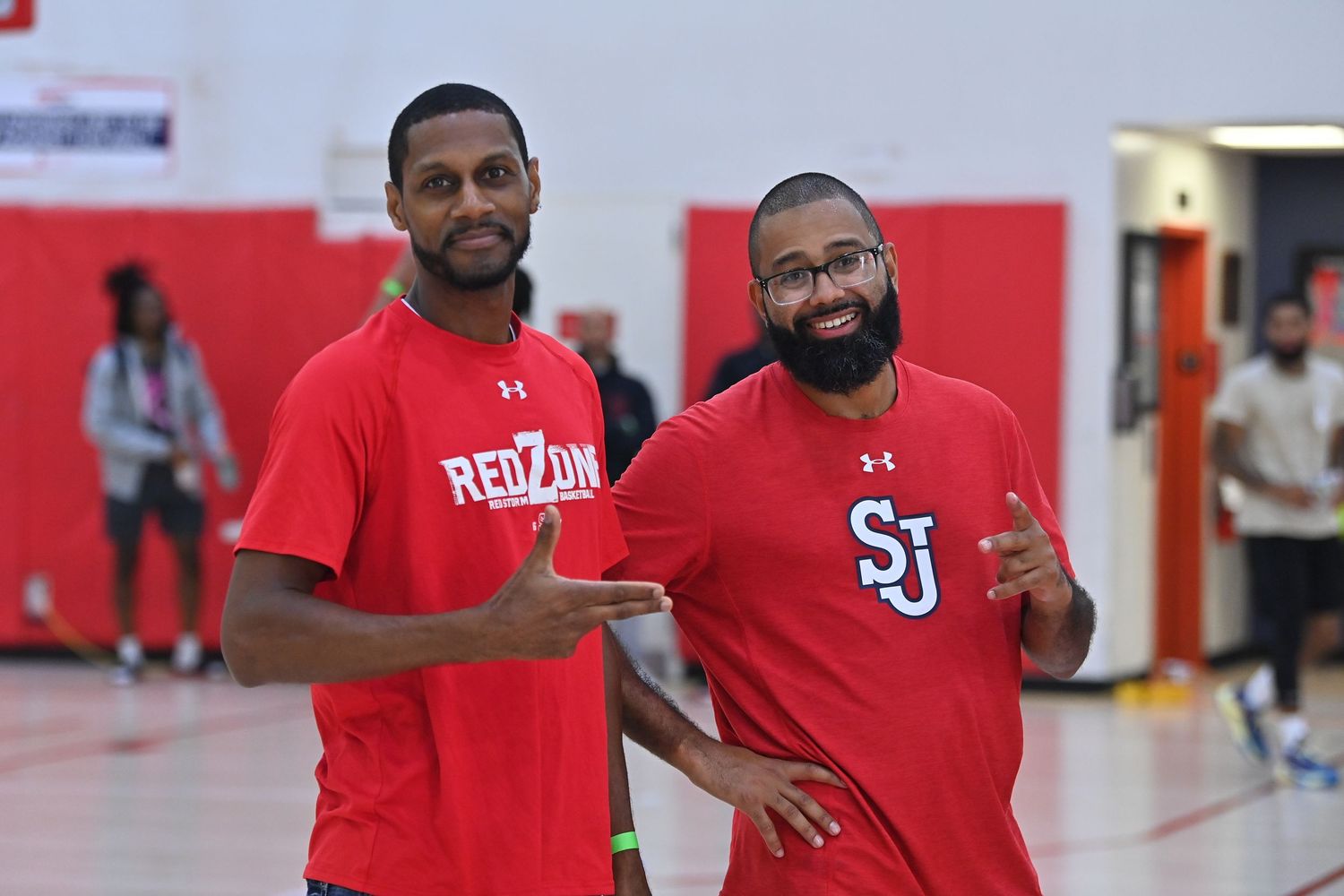 Basketball players and staff in red uniforms gather in a gymnasium during a team practice session.