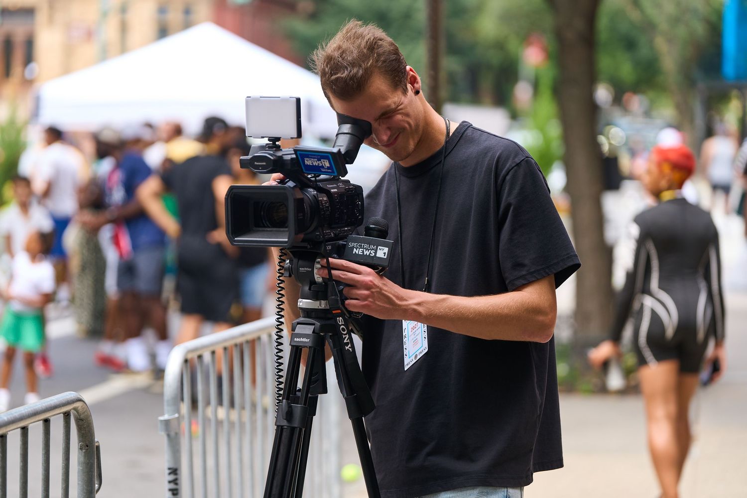 Videographer with professional camera equipment films on a crowded city street during a summer day.