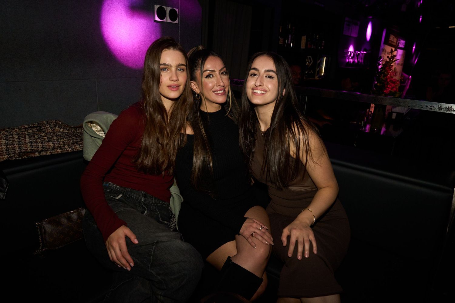 Group of friends dancing and posing together at a nightclub with purple lighting and dark atmosphere.