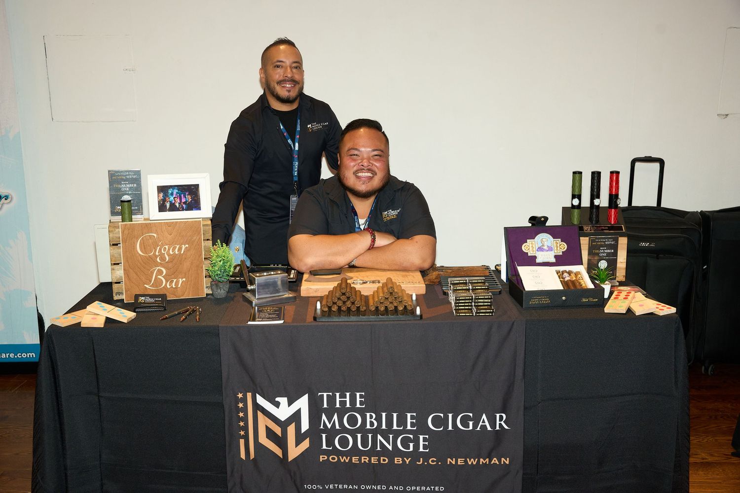 A mobile cigar lounge setup at an event with staff members behind a black-branded counter displaying various cigar products.