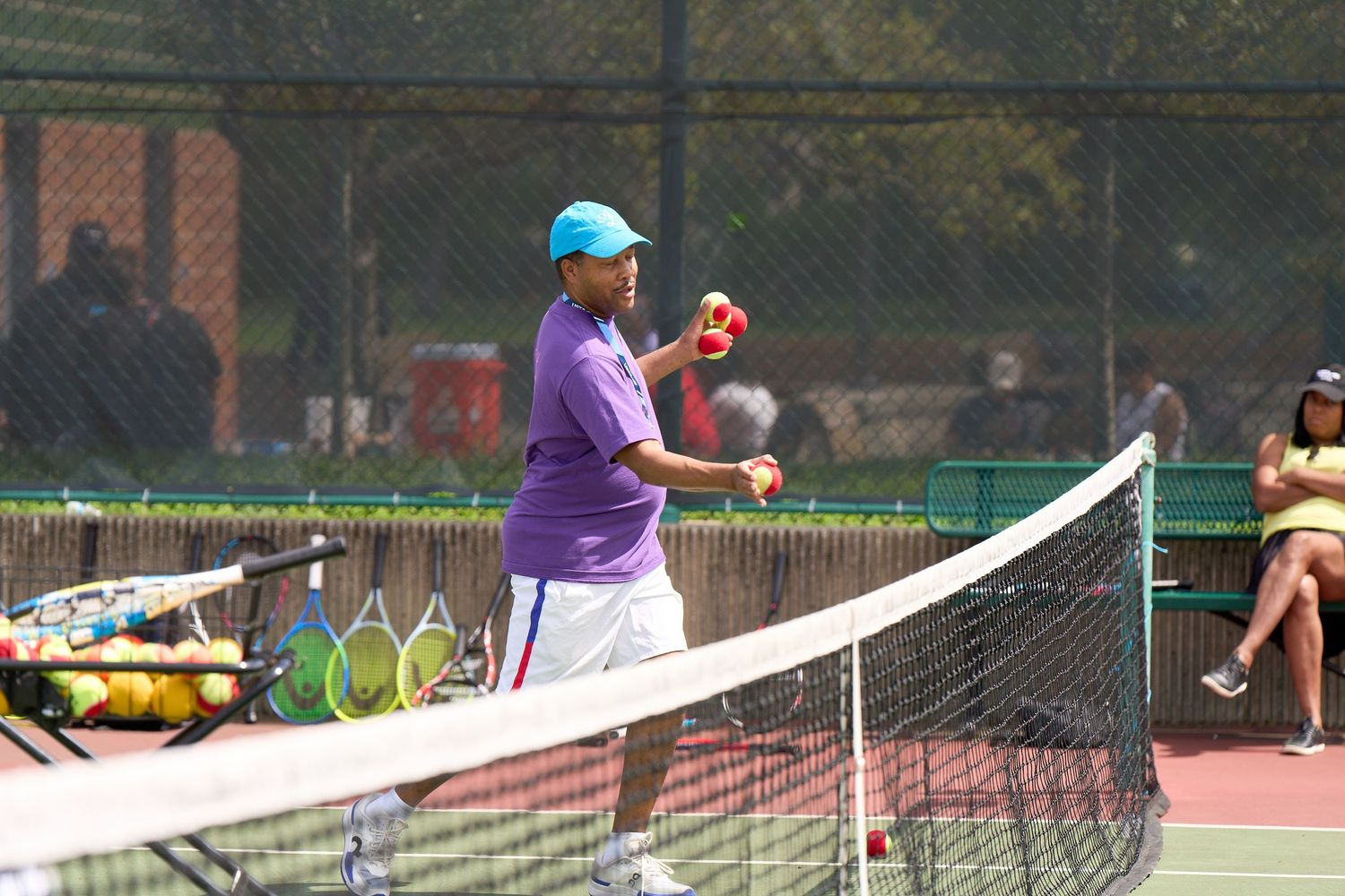 Tennis instructor in purple shirt demonstrates proper form on outdoor court during summer training session.
