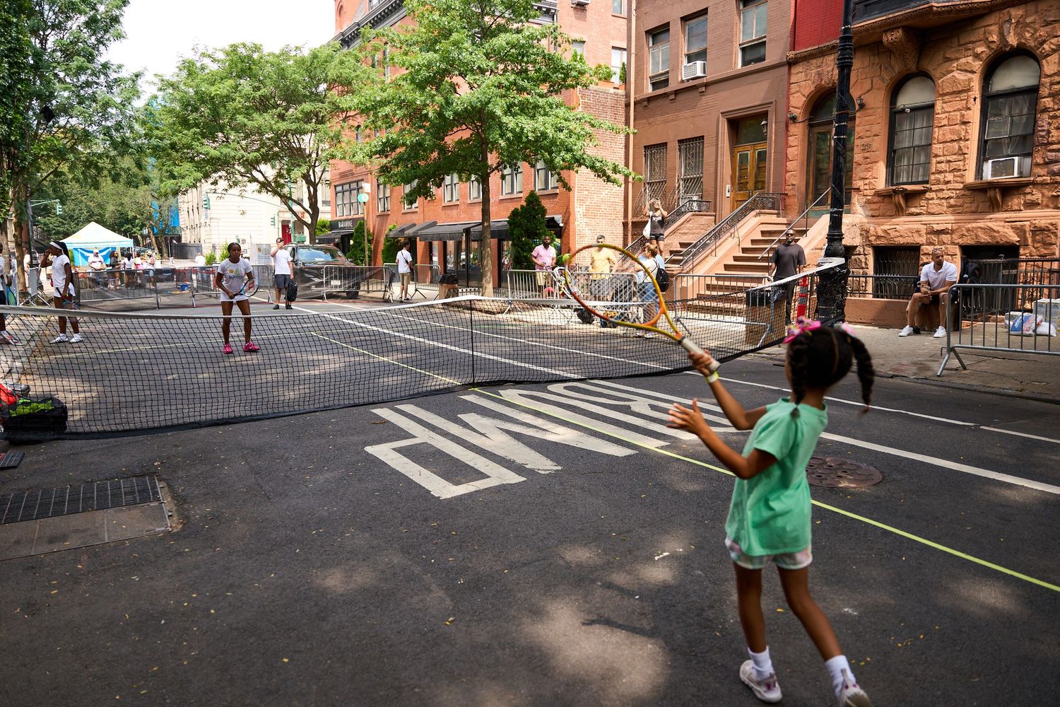 Kids playing in the street of a Brooklyn neighborhood with brownstone buildings and trees in the background.