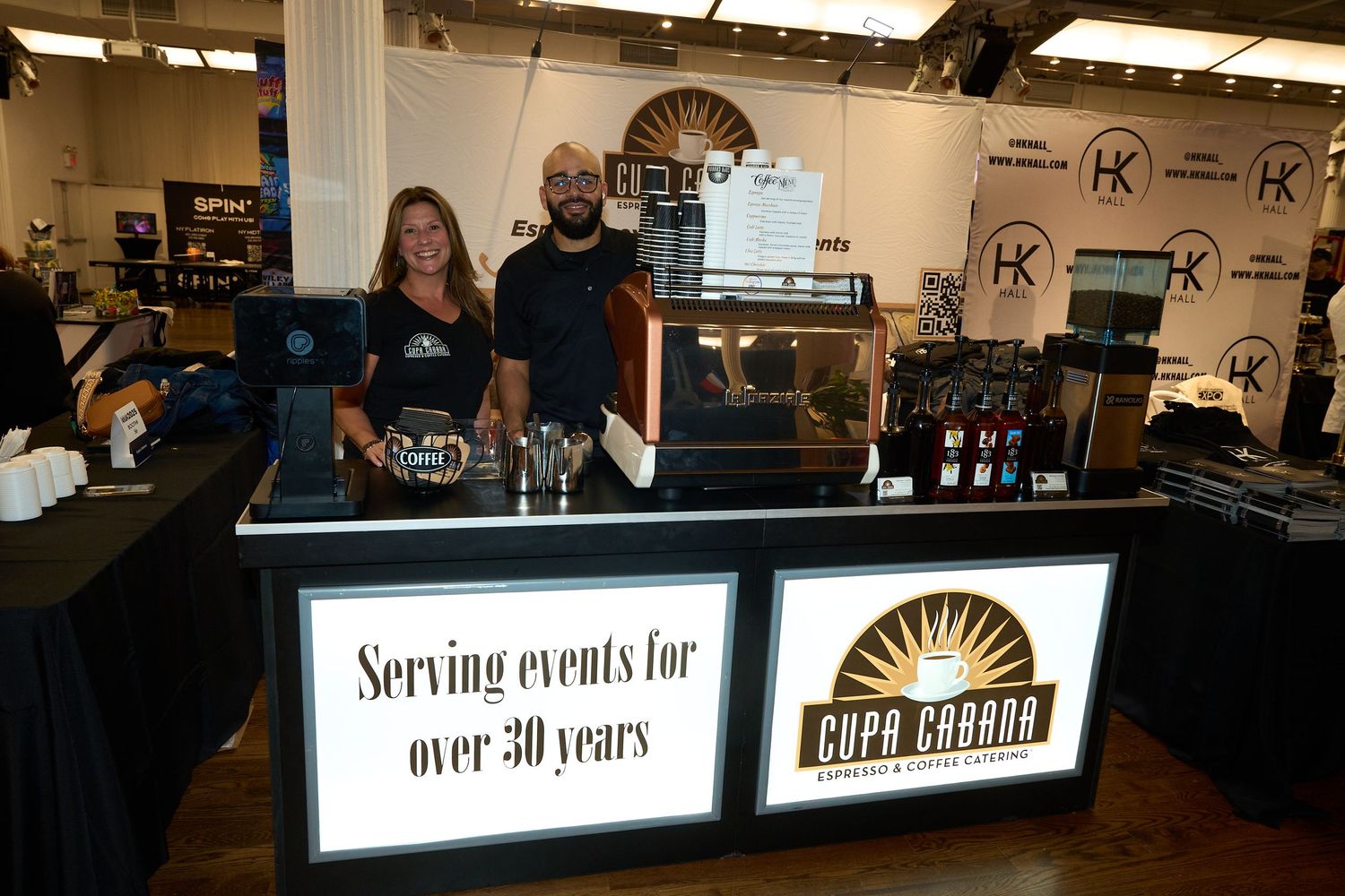 Catering staff stand behind an illuminated bar display with a sign indicating over 50 years of service experience.