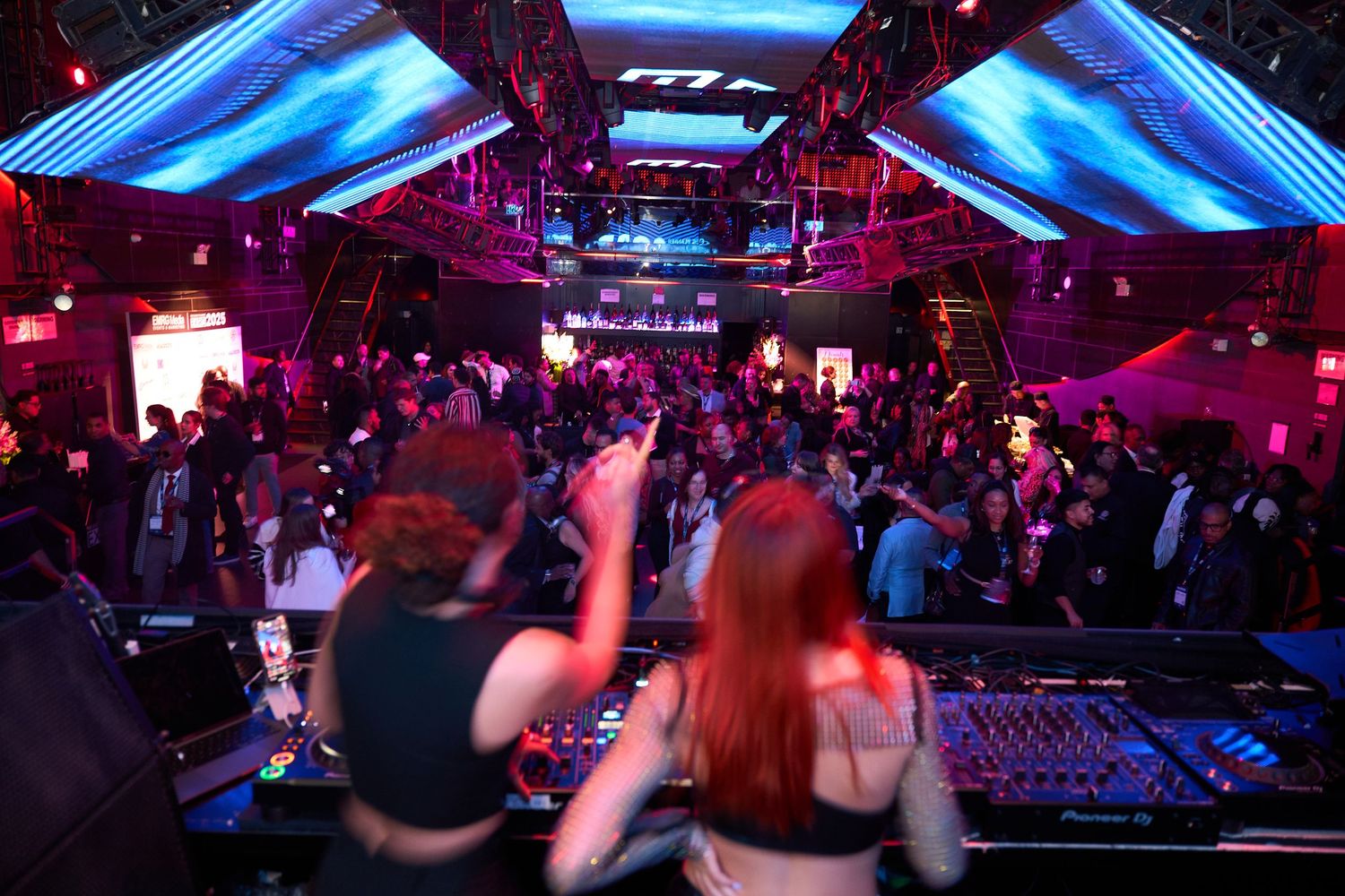Crowded nightclub scene with blue lighting and people dancing on a dark dance floor.