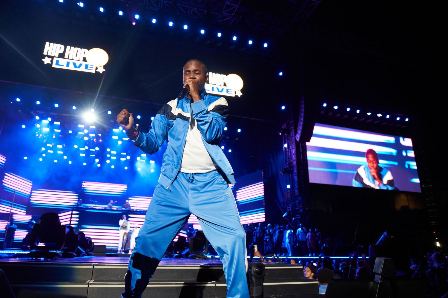 Basketball players wearing light blue uniforms perform on a court with dramatic blue lighting and digital displays.