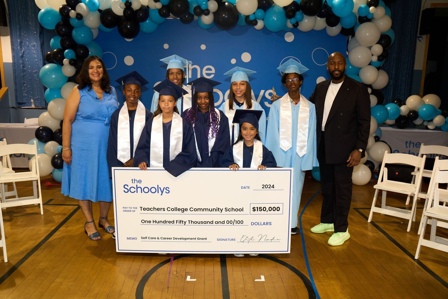Graduation celebration with blue and white balloons, diplomas, and giant novelty check displayed in event space.