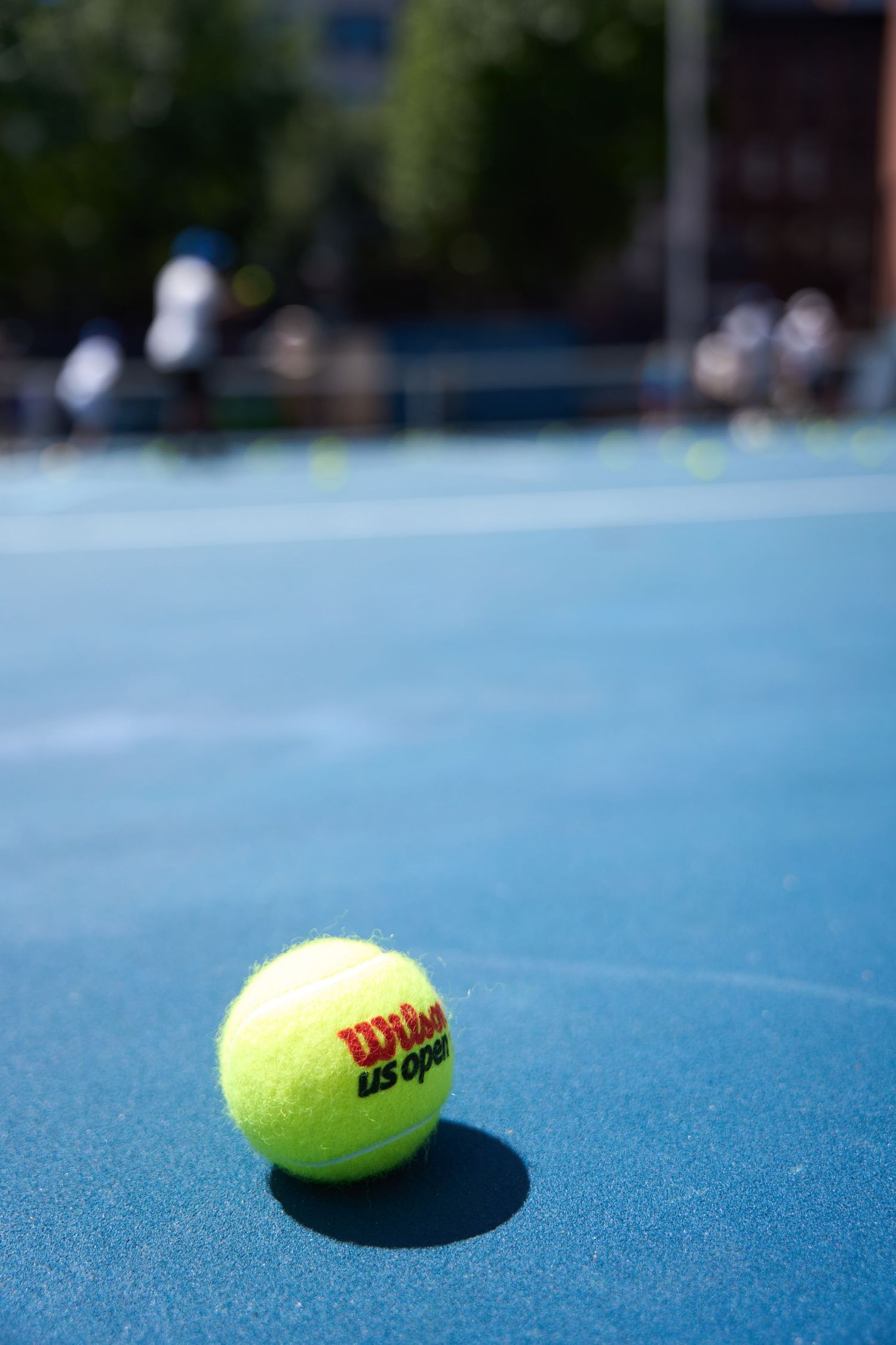 Close-up of a yellow Nike tennis ball casting a shadow on a bright blue tennis court surface.