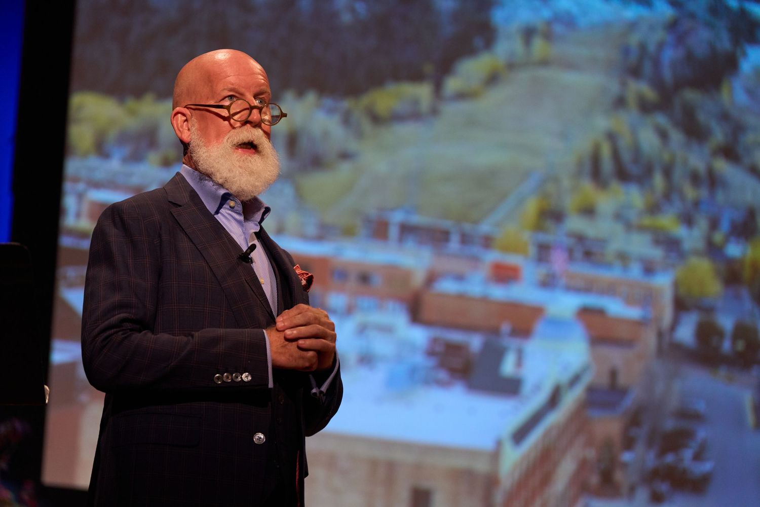 Speaker presenting on stage with projected visuals in a professional conference setting.