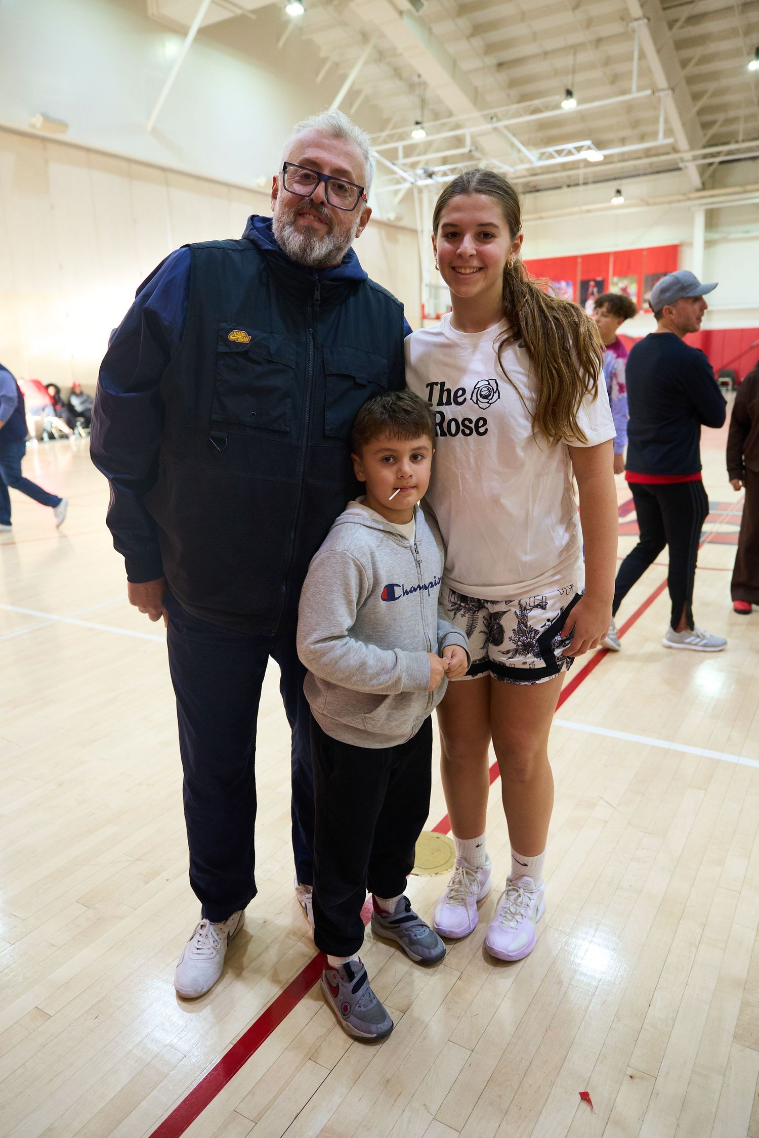Three people pose together on a wooden gymnasium floor with red lines and bright overhead lighting.