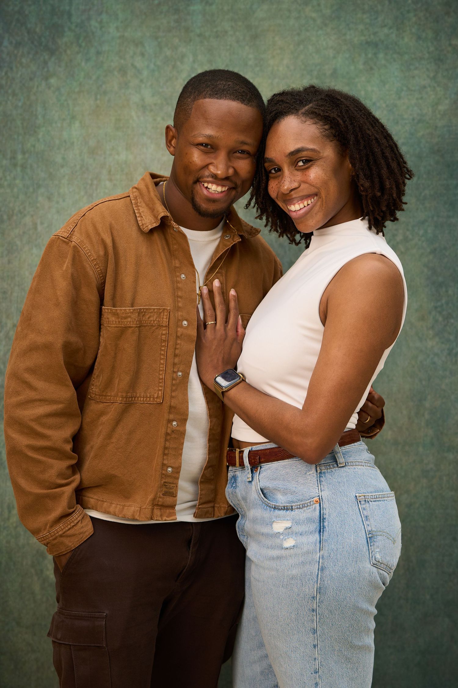 A couple sharing tender loving moments in matching brown and white outfits against a textured green backdrop.