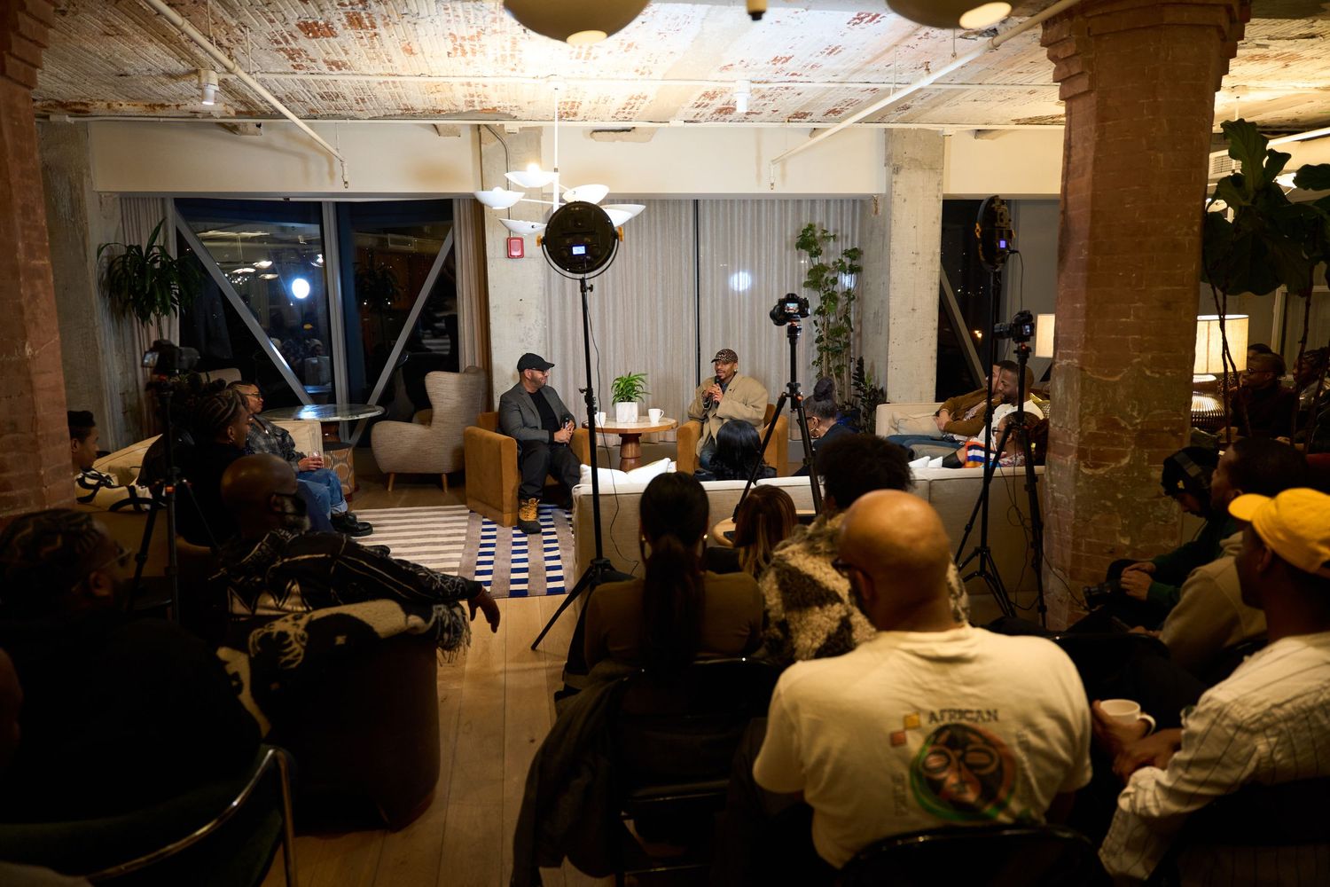 Musicians perform on stage at an intimate concert venue with exposed brick walls and a seated audience.