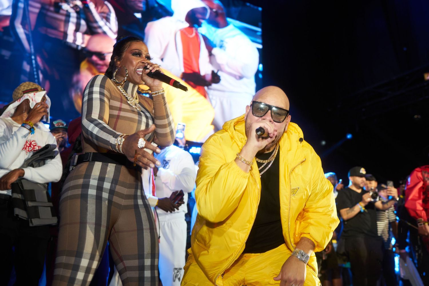 Performers wearing colorful outfits sing energetically on stage during a concert with blue lighting in the background.