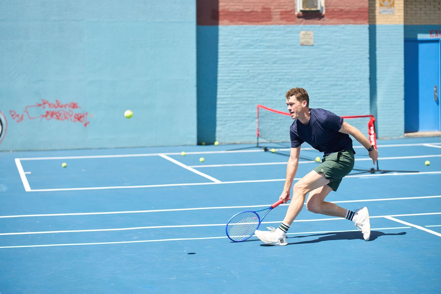 Players engage in an intense pickleball rally on a bright blue outdoor sports court.