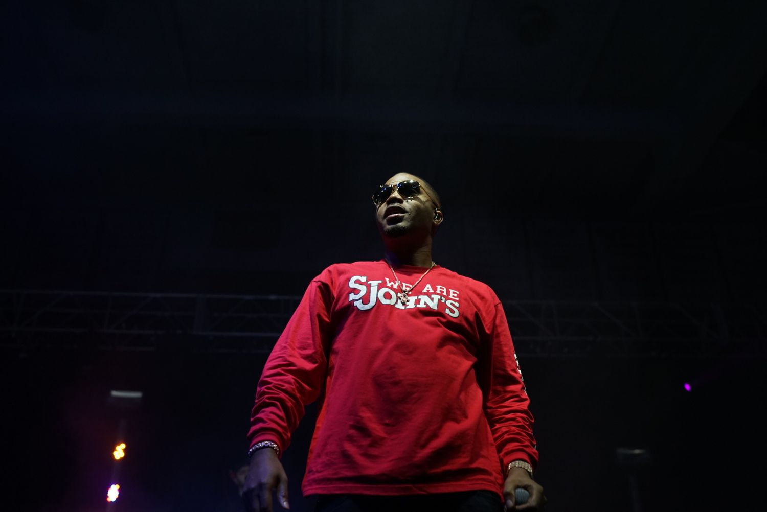 A performer in a red sweatshirt stands on a dimly lit stage during a performance.