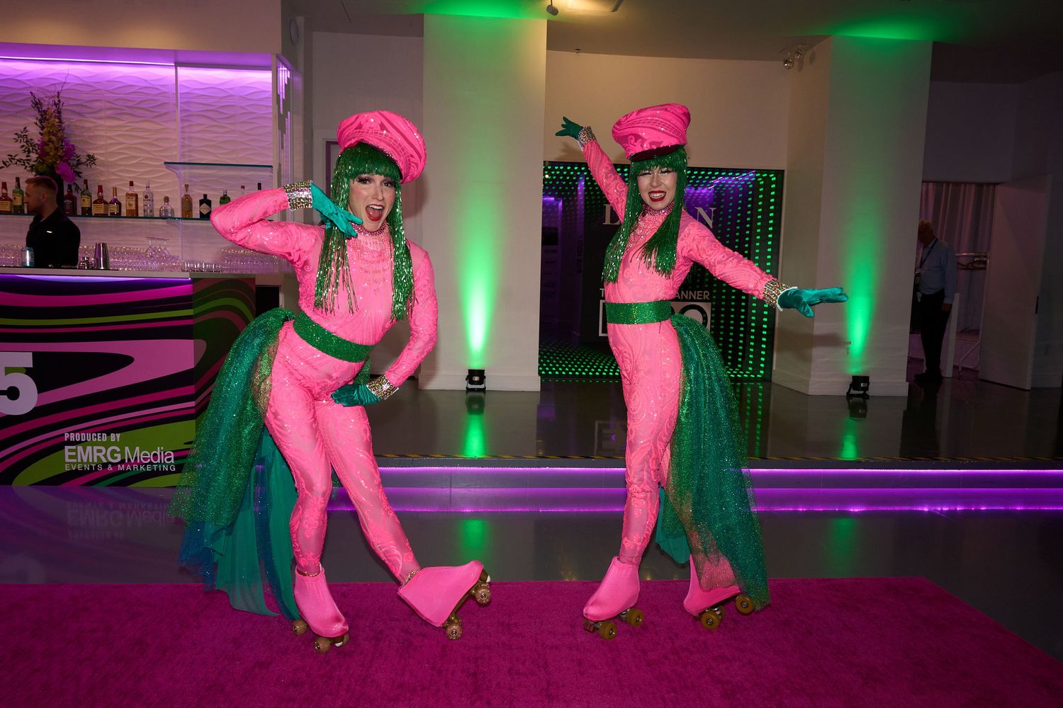 Dancers perform energetic choreography in a room with pink and green lighting effects on the dance floor.