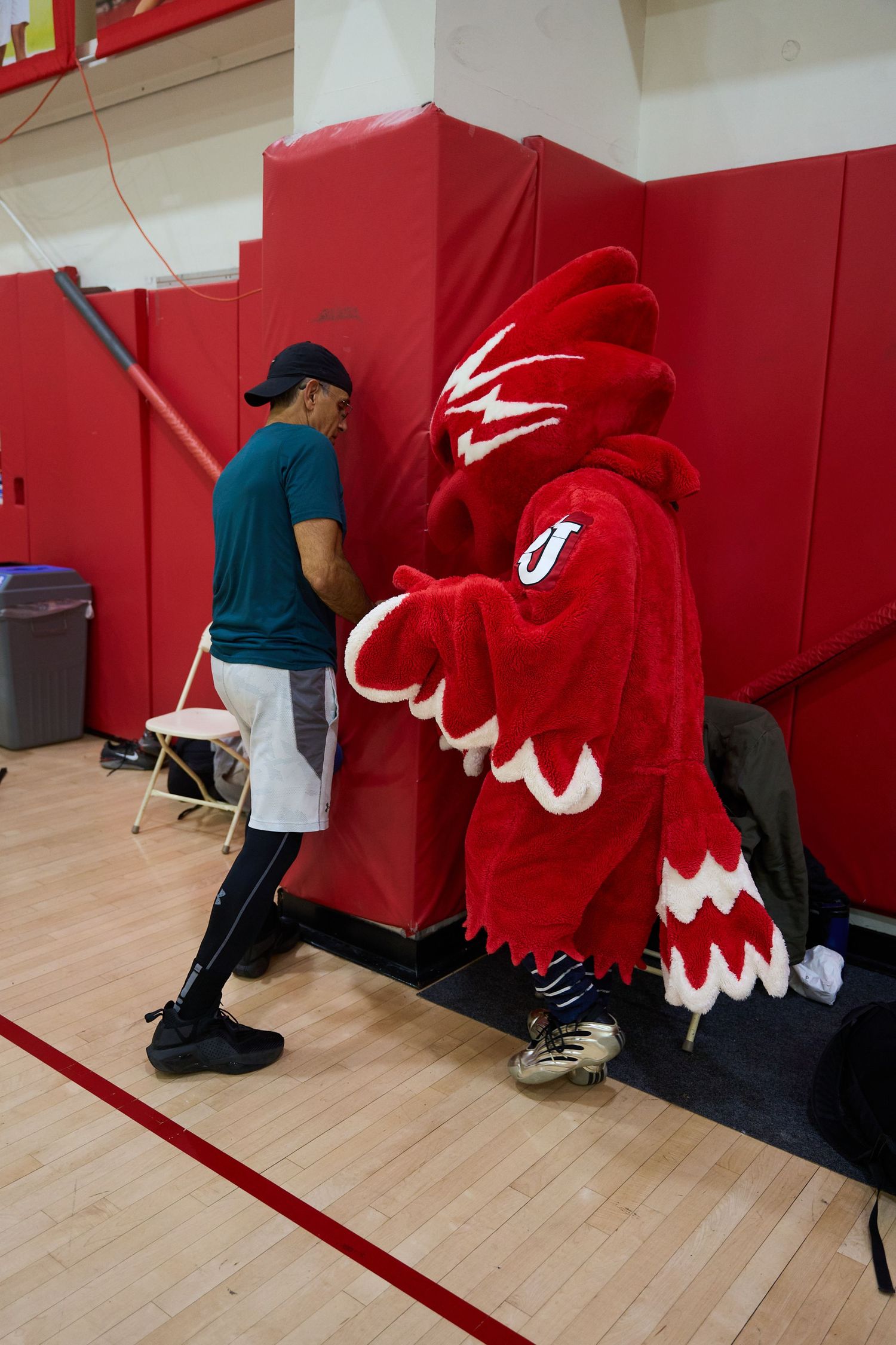 Red mascot costume lying on wooden gym floor with black stripes.