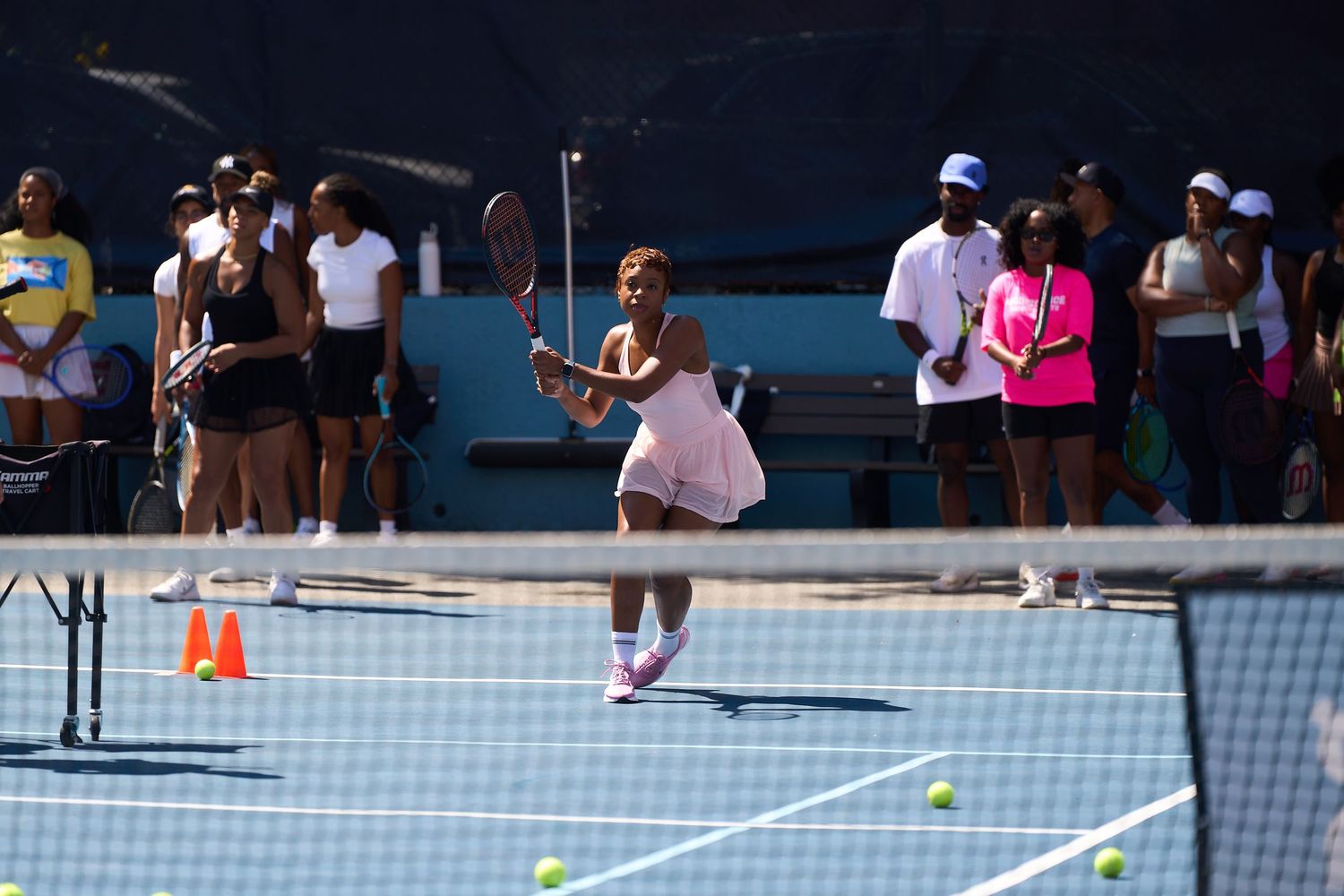 Multiple tennis players training on blue courts with spectators watching from the sidelines.