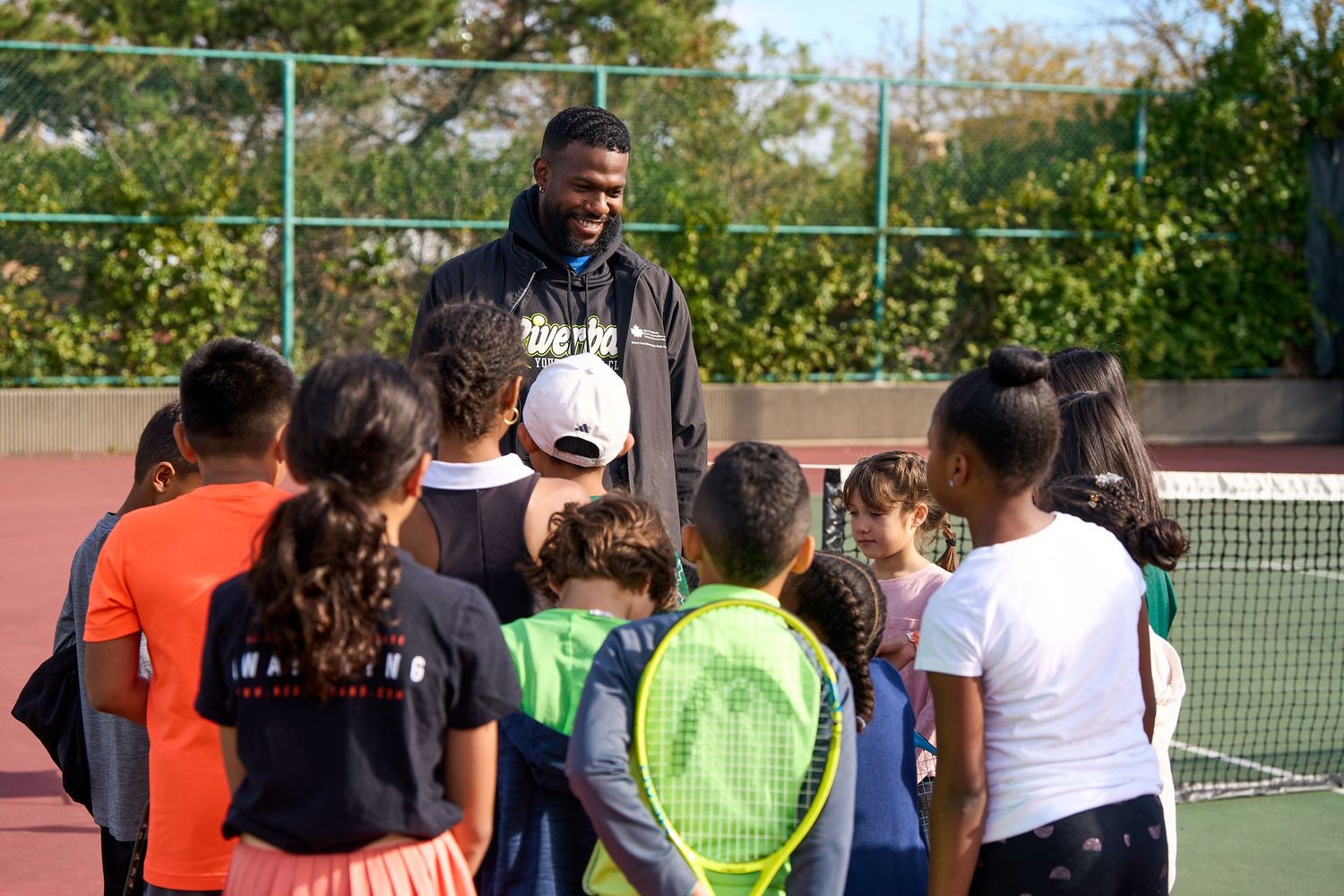 Group of tennis players gathered on outdoor courts during a sunny day for training or instruction.
