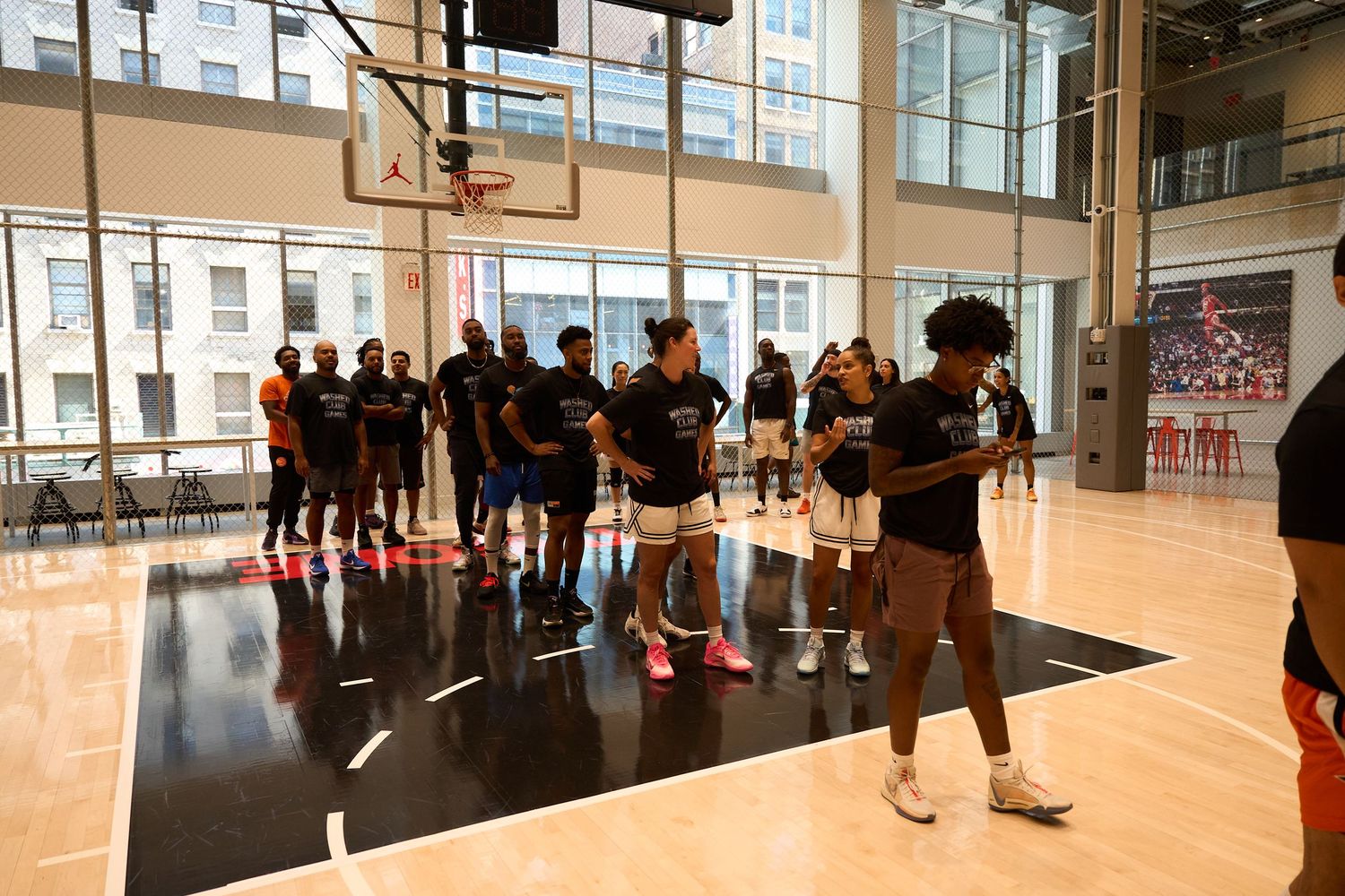 Wide angle panorama view of a bright indoor basketball court with players practicing and spectators along the sides.