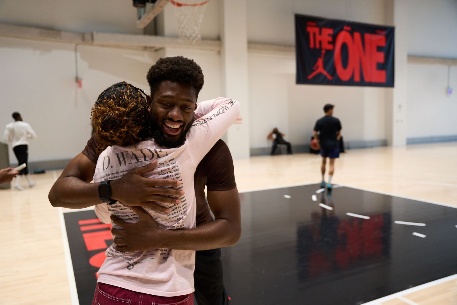 Basketball players embracing on court during an indoor game session with 'ONE' banner visible in background.