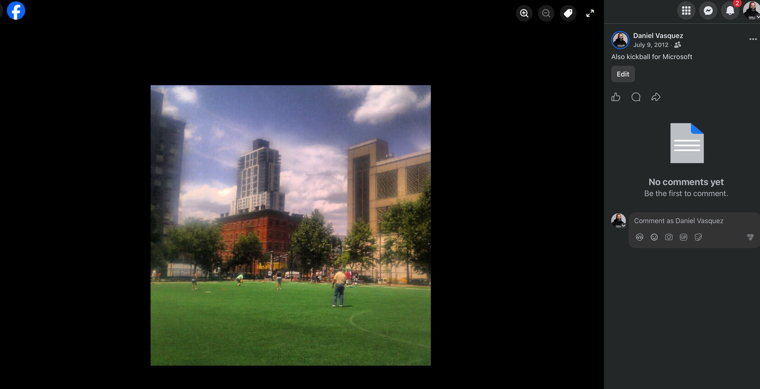 Person standing on a green grass lawn in a city park with tall brick and glass buildings under a blue sky with clouds.