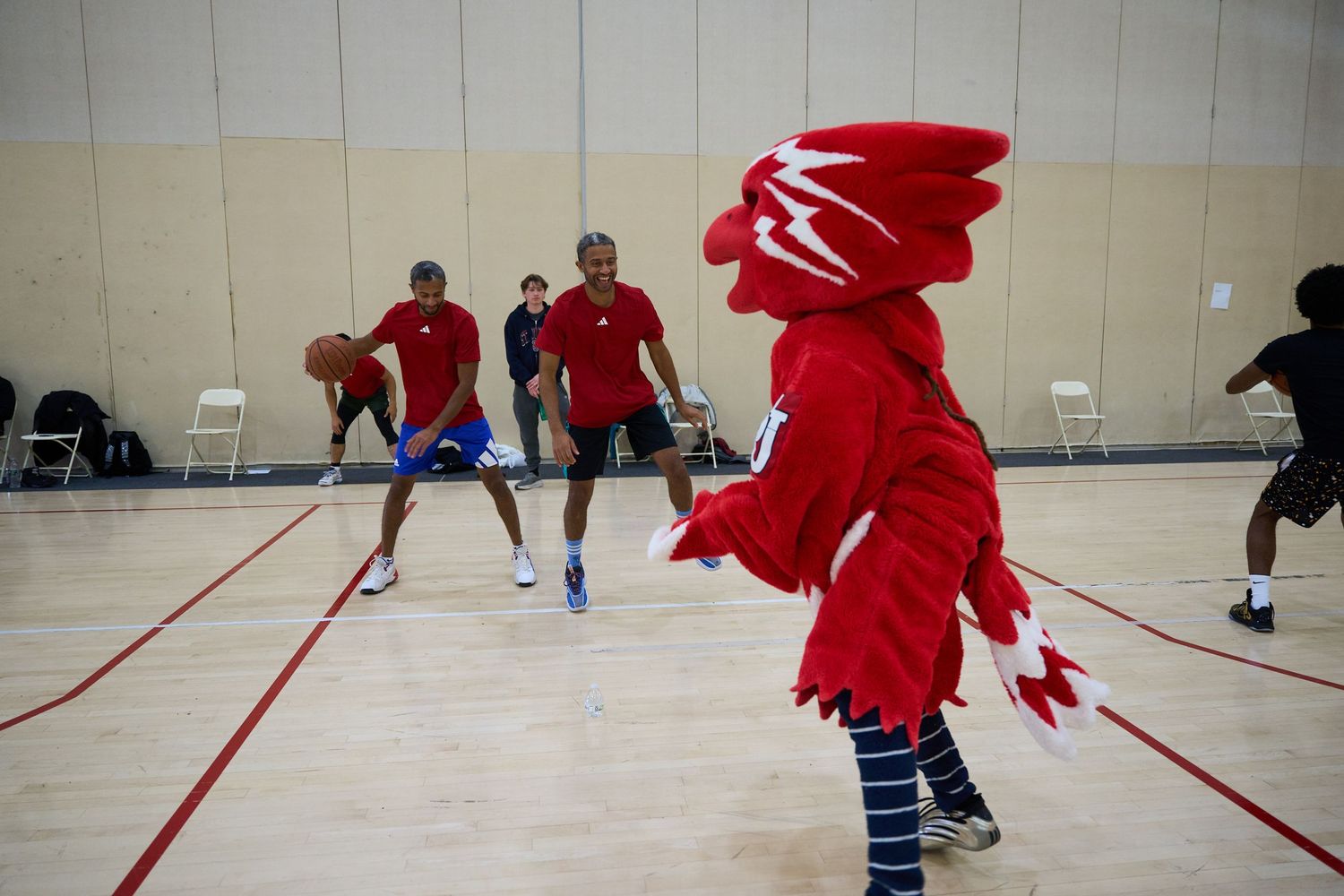 Athletes in red jerseys practice drills on an indoor gymnasium court with white floor markings.